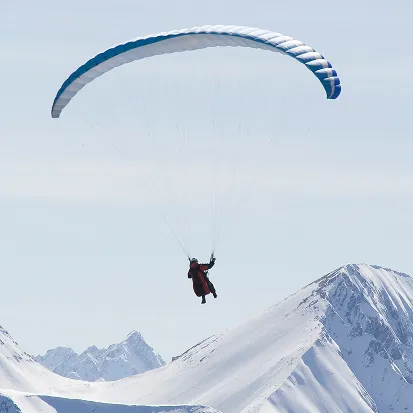 Personne en parapente volant au-dessus de montagnes enneigées sous un ciel clair, La Ferme des Drus, Chamonix-Mont-Blanc, France.