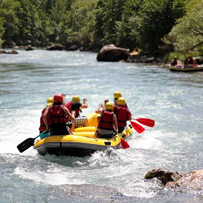 Groupe en raft jaune pagayant sur une rivière entourée d'arbres et de rochers, La Ferme des Drus, Chamonix-Mont-Blanc, France.