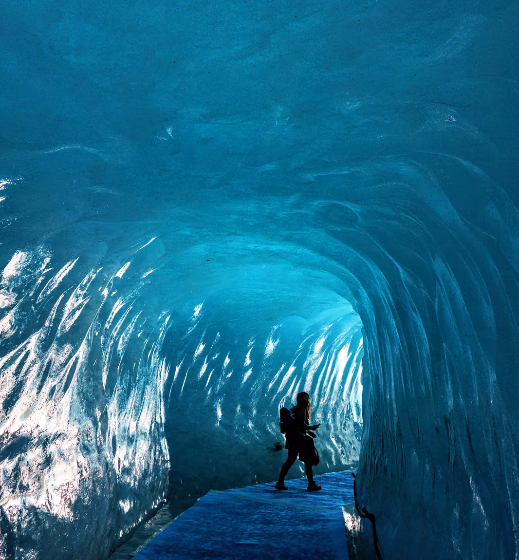 Personne marchant à l'intérieur d'une grotte de glace d'un bleu lumineux, aux parois et au plafond texturés, à La Ferme des Drus, Chamonix-Mont-Blanc, France.