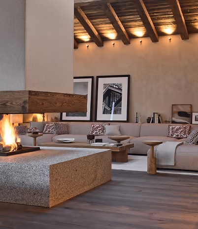 Salon moderne avec canapés beiges, cheminée centrale en pierre, poutres en bois au plafond, La Ferme des Drus, Chamonix-Mont-Blanc, France.