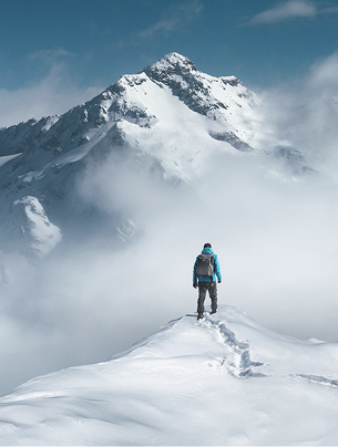 Personne debout sur un sommet enneigé, contemplant une haute montagne couverte de neige sous un ciel bleu parsemé de nuages, La Ferme des Drus, Chamonix-Mont-Blanc, France.