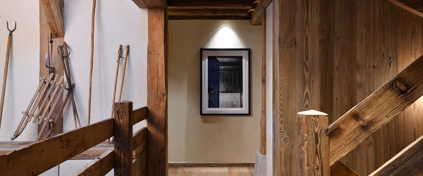 Intérieur rustique en bois avec un cadre photo éclairé montrant une porte bleue ouverte dans une pièce sombre, La Ferme des Drus, Chamonix-Mont-Blanc, France.