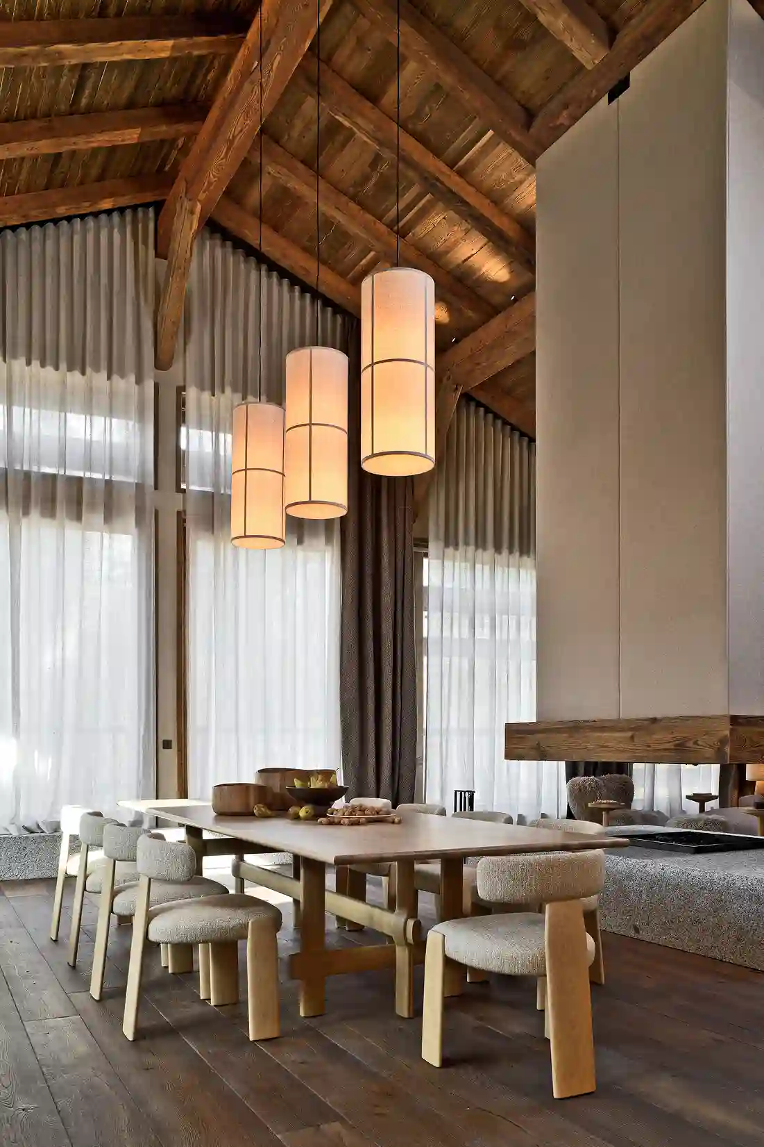 Salle à manger moderne en bois avec table, chaises, lustres cylindriques et plafond en poutres apparentes, La Ferme des Drus, Chamonix-Mont-Blanc, France.