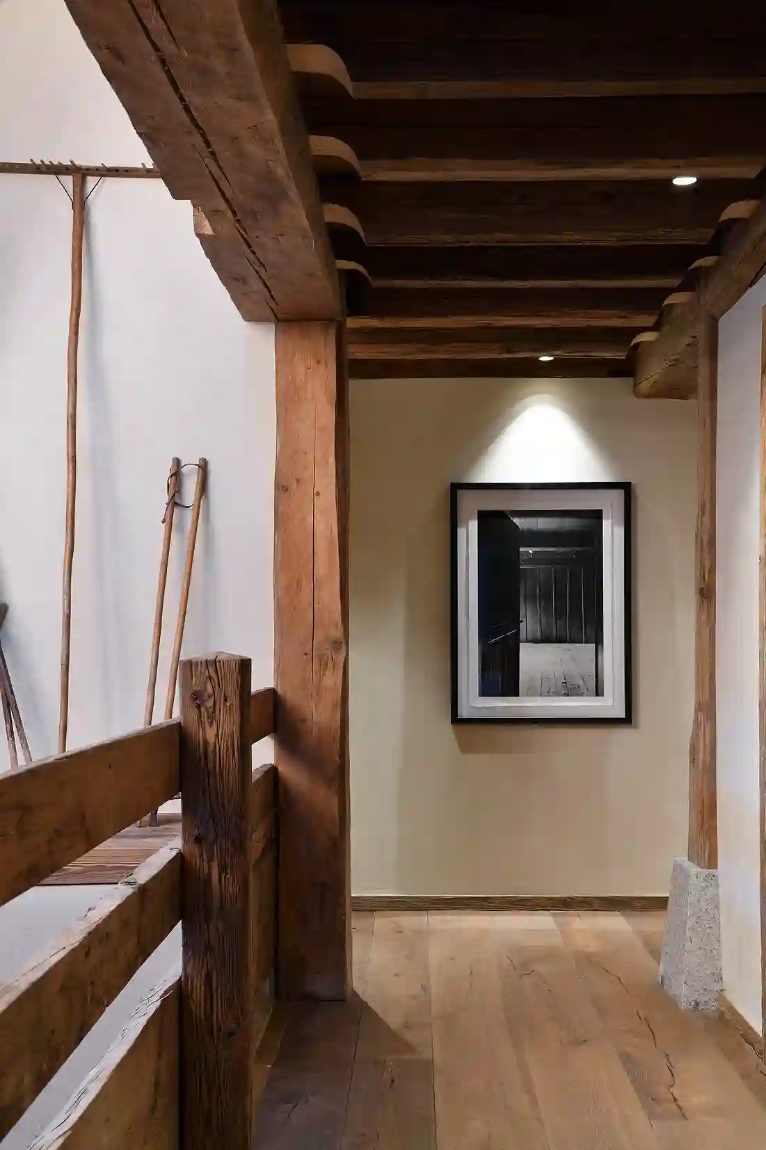 Couloir avec poutres en bois, parquet clair et un tableau noir éclairé sur un mur beige, La Ferme des Drus, Chamonix-Mont-Blanc, France.