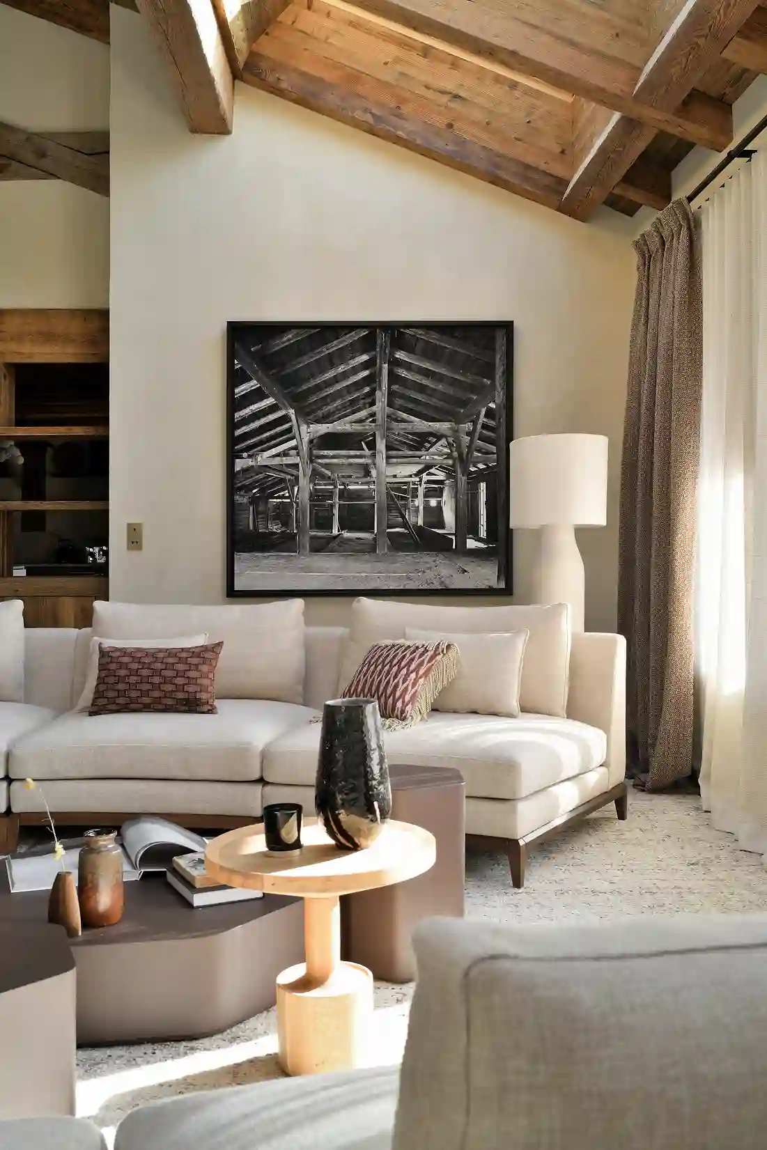 Salon moderne avec canapé beige, table basse en bois, et tableau noir-blanc d’une charpente en bois, La Ferme des Drus, Chamonix-Mont-Blanc, France.