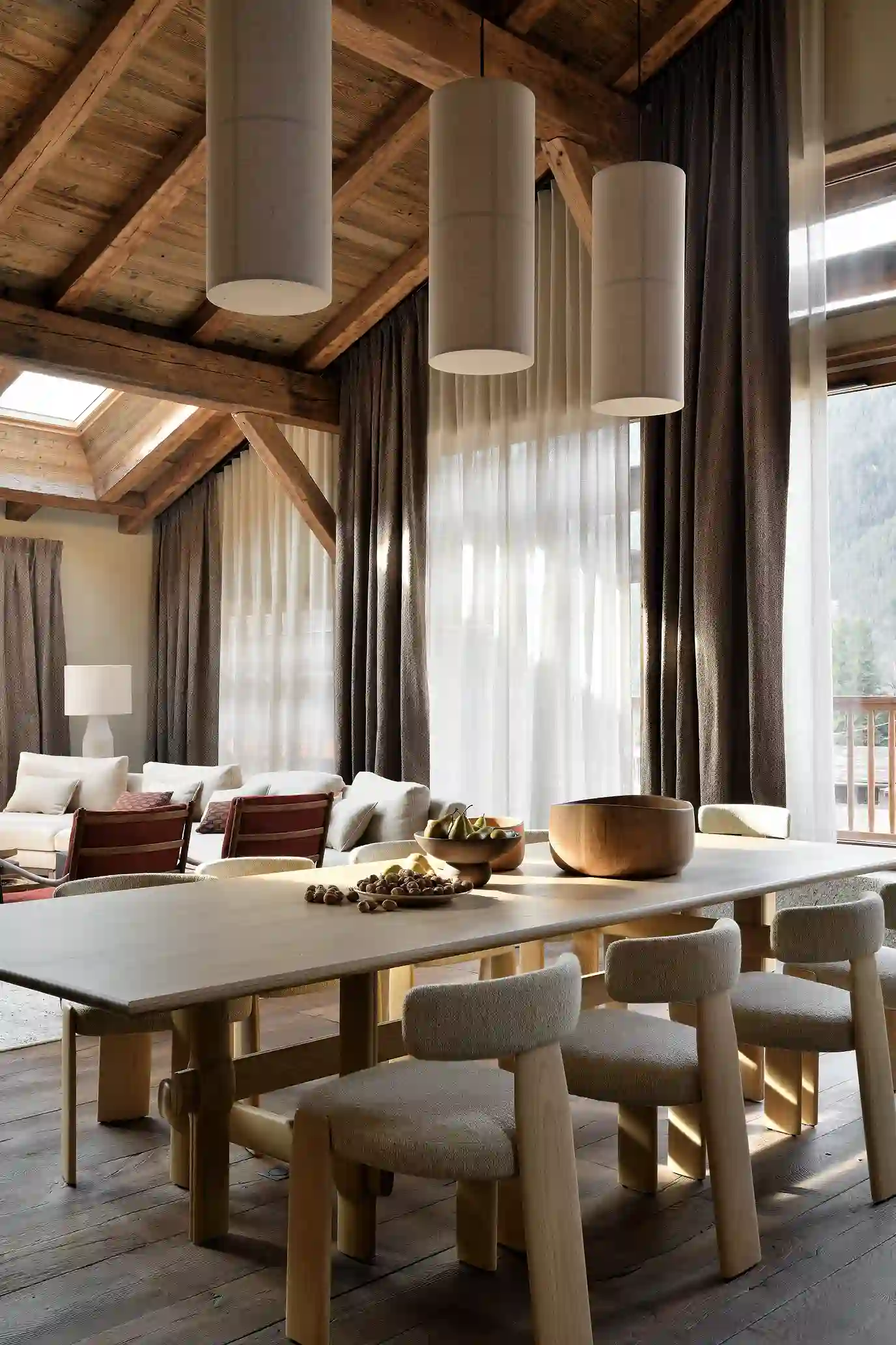Salle à manger avec grande table en bois, chaises rembourrées, suspensions cylindriques et poutres apparentes, La Ferme des Drus, Chamonix-Mont-Blanc, France.