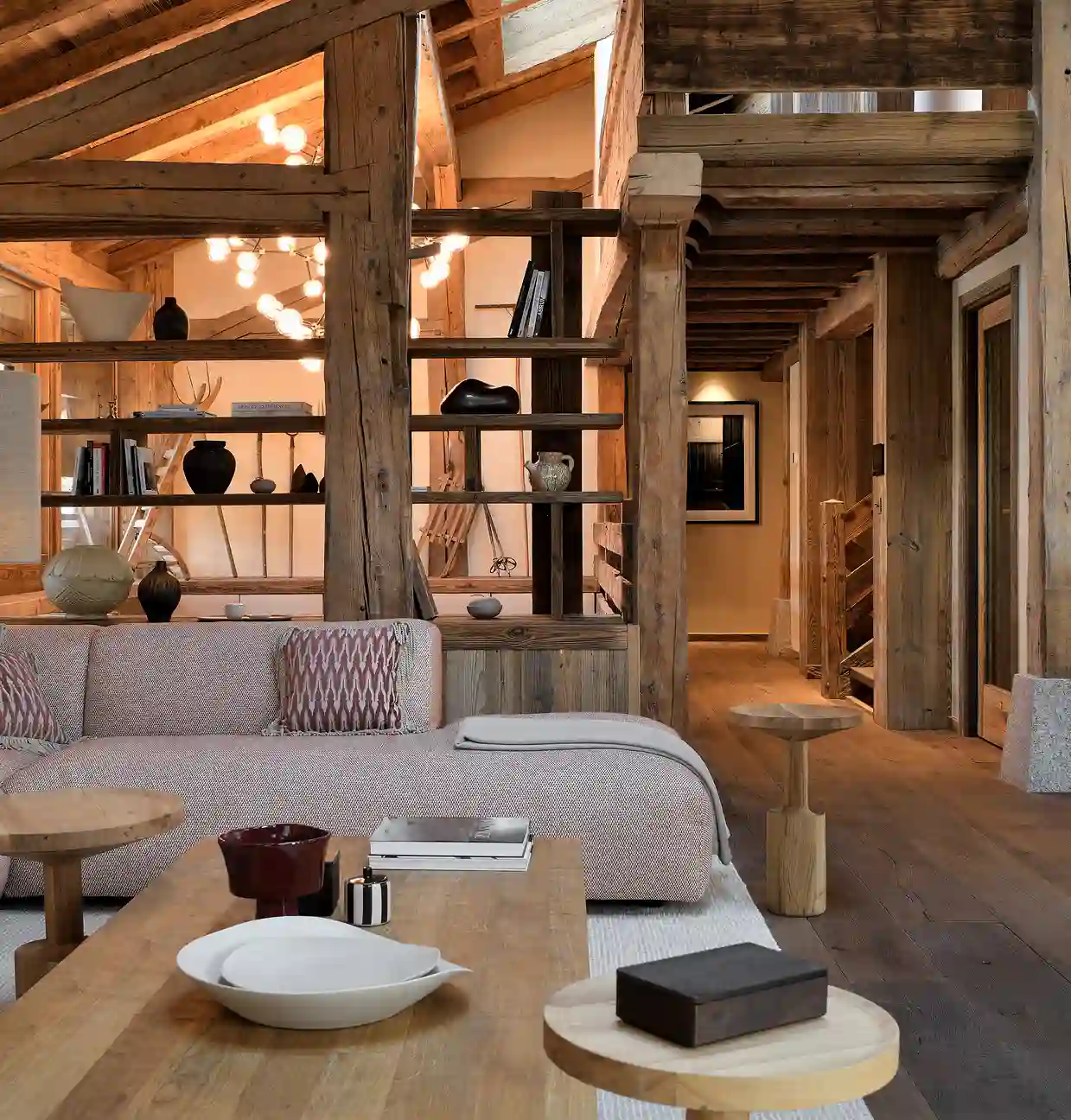 Salon moderne avec canapés, tables en bois, étagères ouvertes et murs en bois rustique, La Ferme des Drus, Chamonix-Mont-Blanc, France.