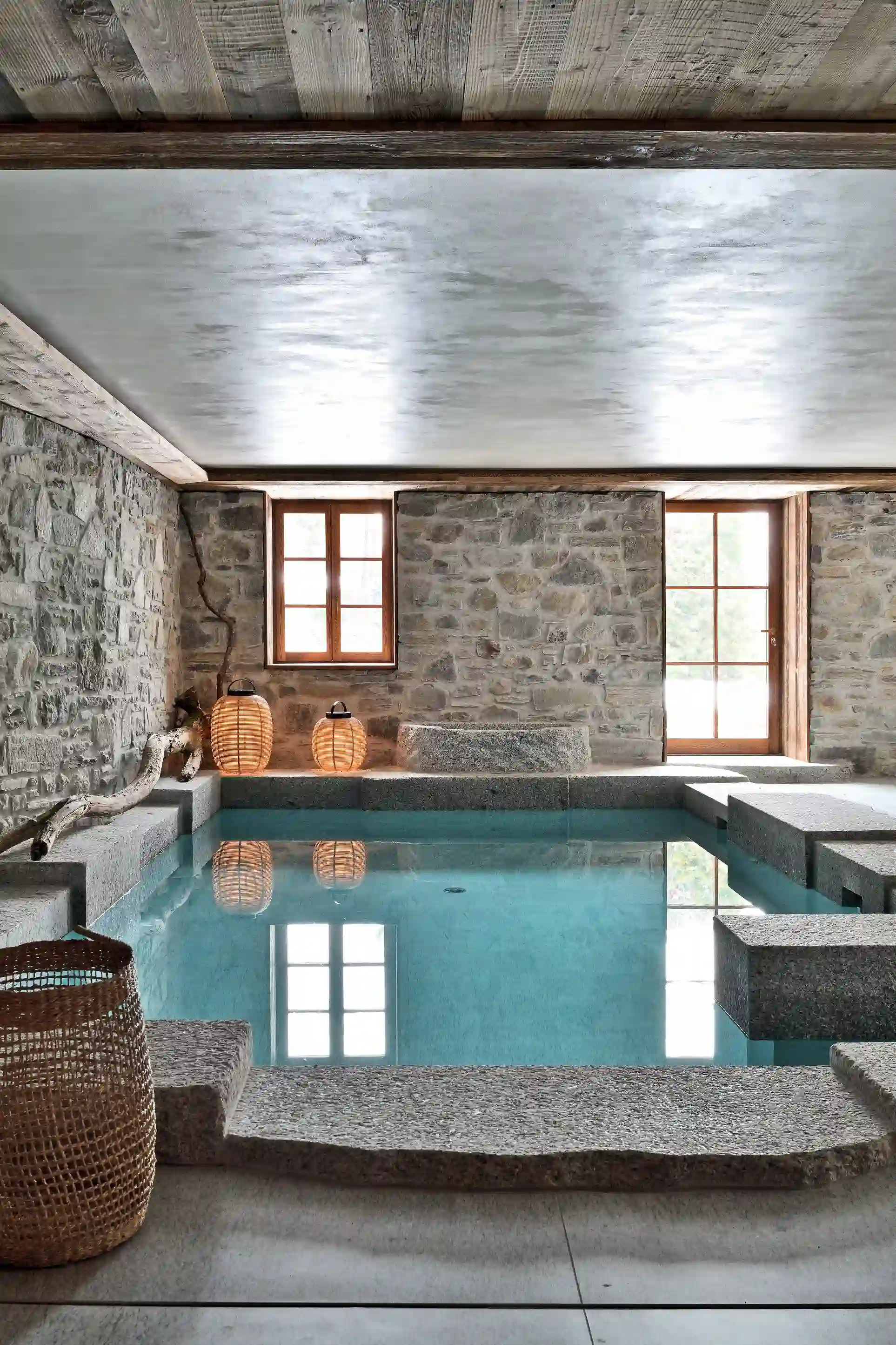 Piscine intérieure avec murs en pierre, fenêtres en bois, lanternes en osier et paniers tressés, La Ferme des Drus, Chamonix-Mont-Blanc, France.