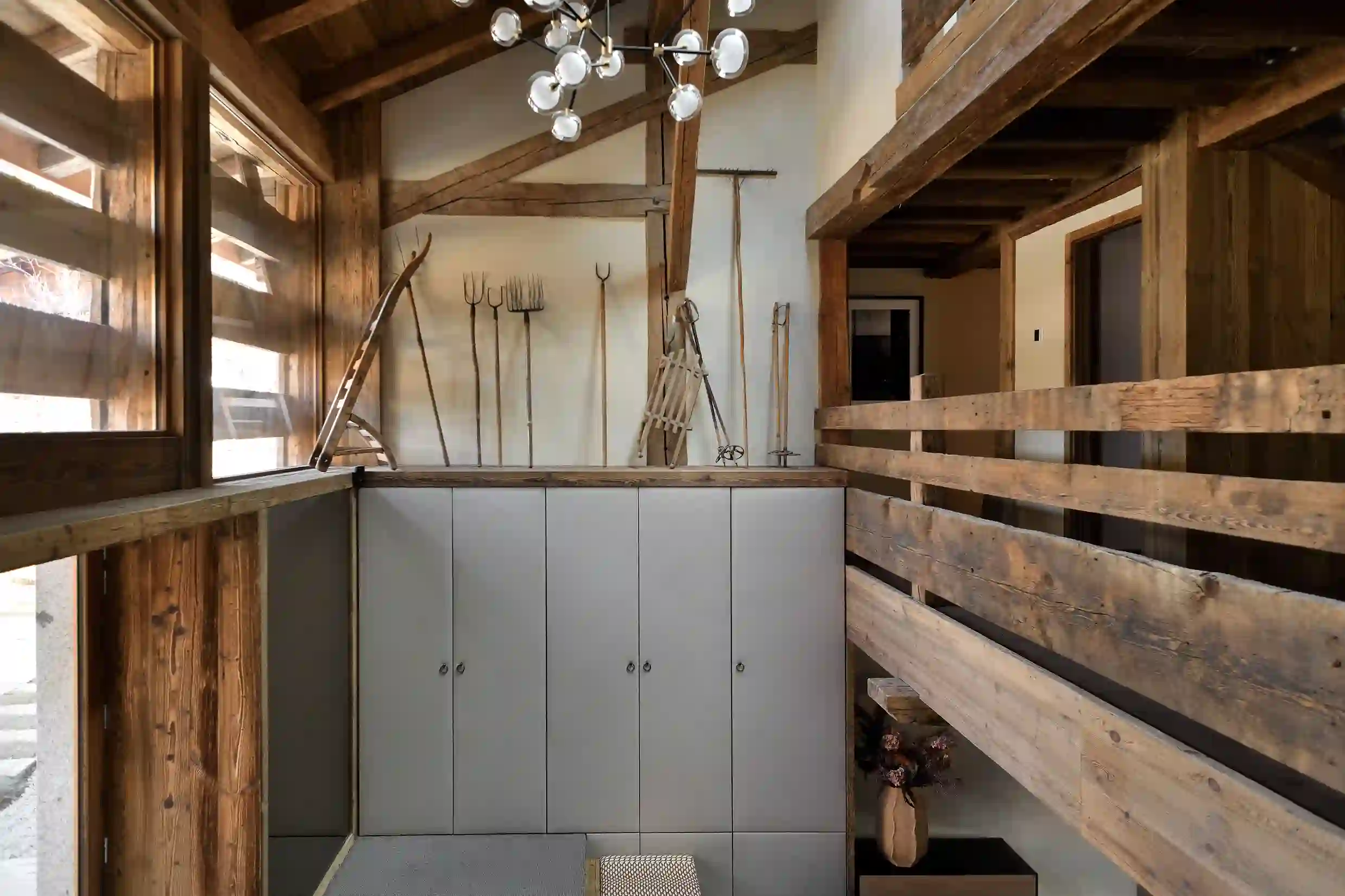 Intérieur en bois avec outils agricoles suspendus et grand meuble gris sous un plafond à poutres, La Ferme des Drus, Chamonix-Mont-Blanc, France.