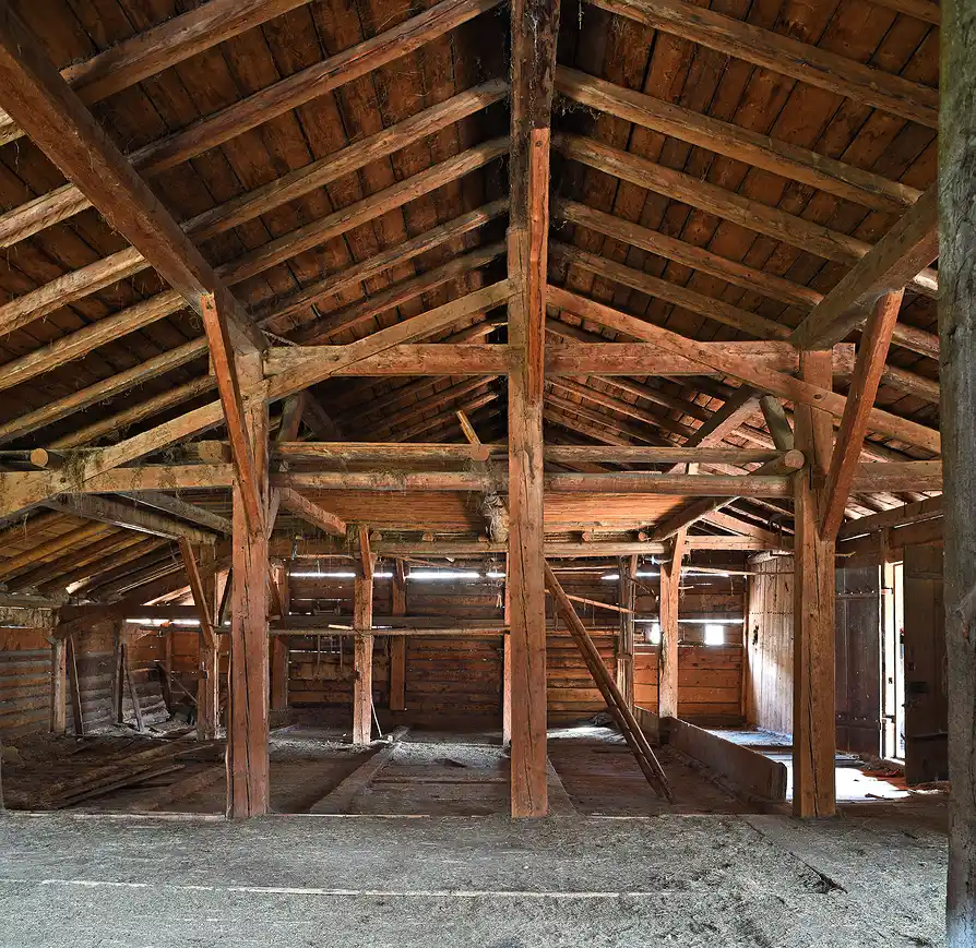 Intérieur d'une grange ancienne avec une charpente en bois et un sol en terre battue, La Ferme des Drus, Chamonix-Mont-Blanc, France.