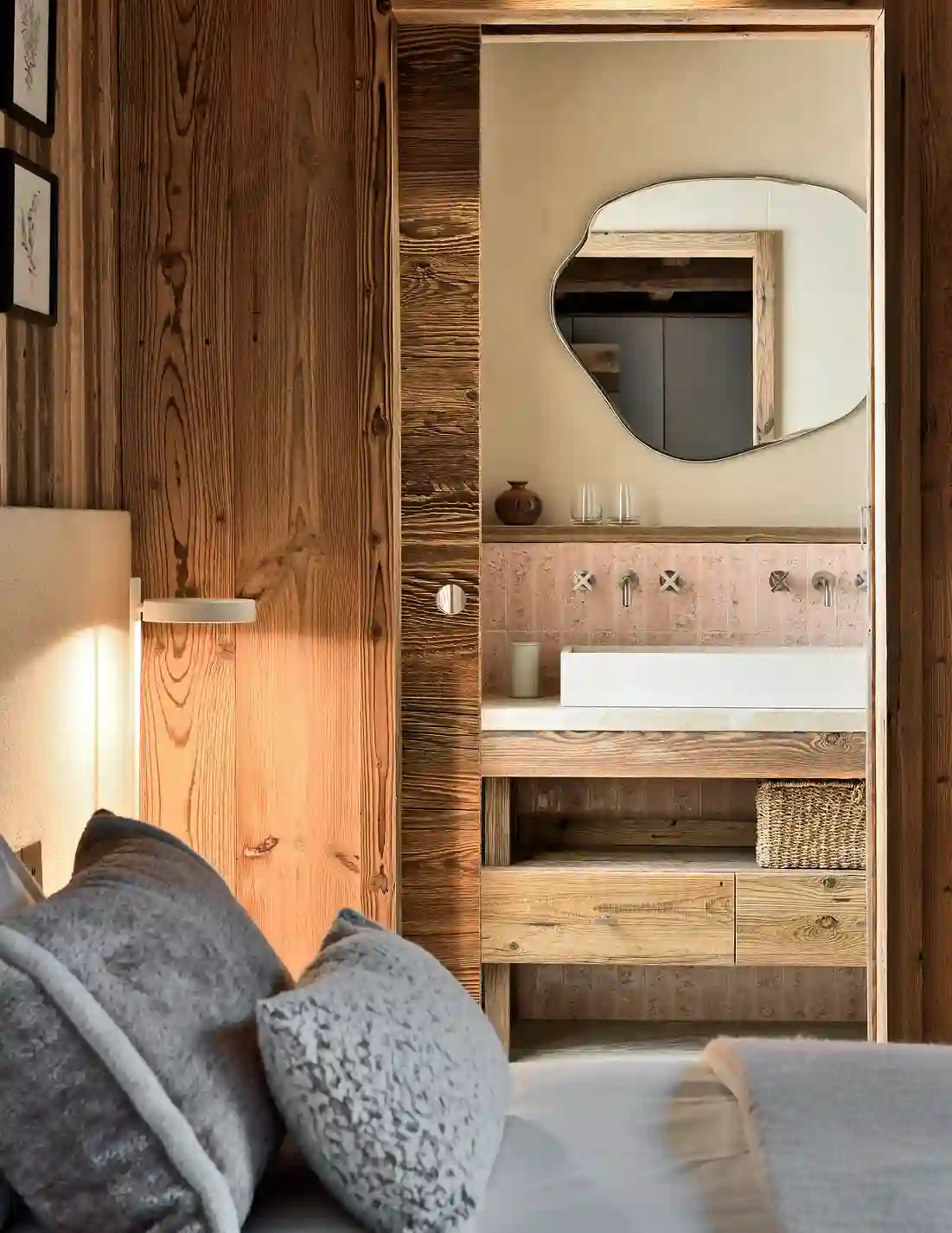 Vue partielle d'une chambre avec oreillers gris et salle de bain en bois avec miroir unique, La Ferme des Drus, Chamonix-Mont-Blanc, France.