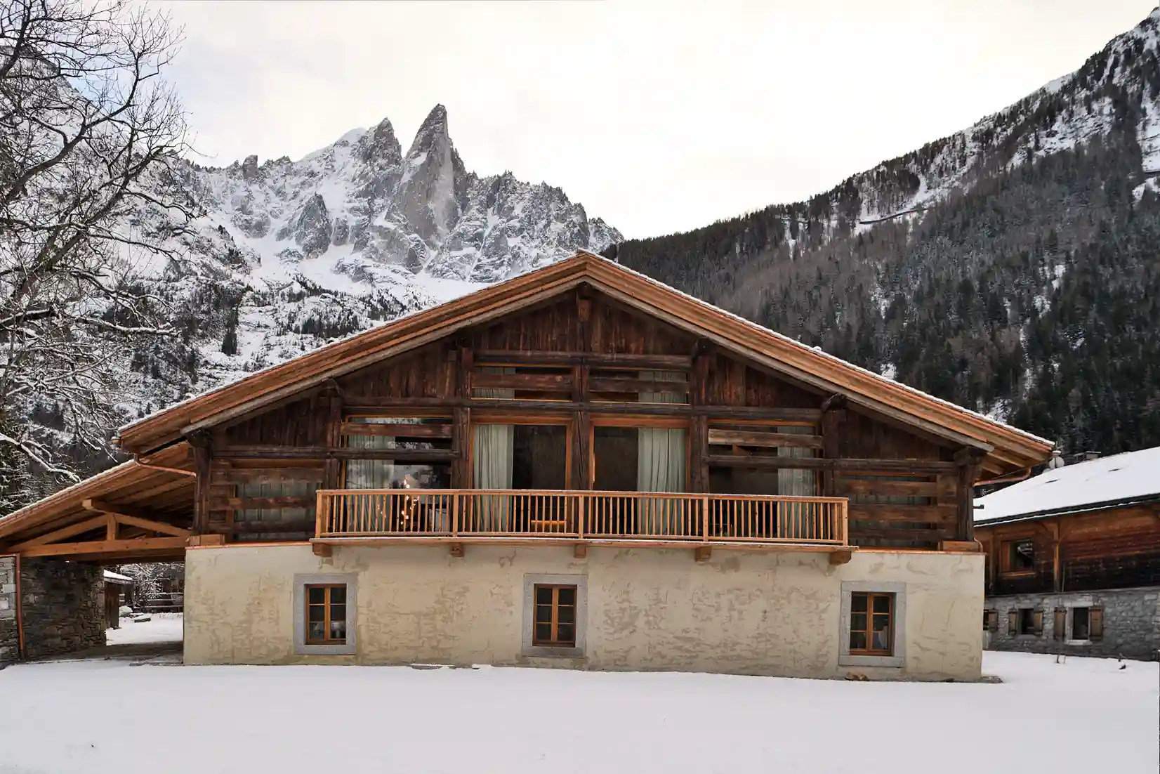 Chalet en bois avec neige et montagnes enneigées en arrière-plan par temps nuageux, La Ferme des Drus, Chamonix-Mont-Blanc, France.