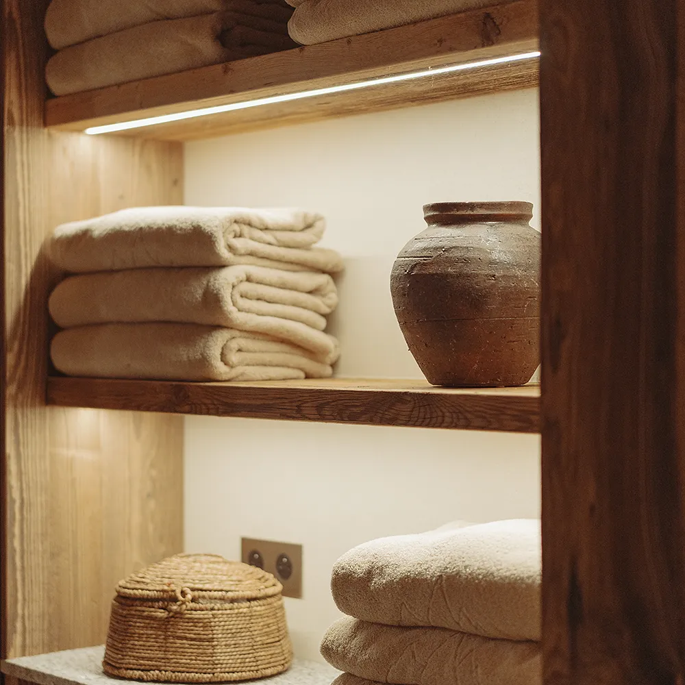 Serviettes pliées beige et pot en argile sur des étagères en bois éclairées, La Ferme des Drus, Chamonix-Mont-Blanc, France.