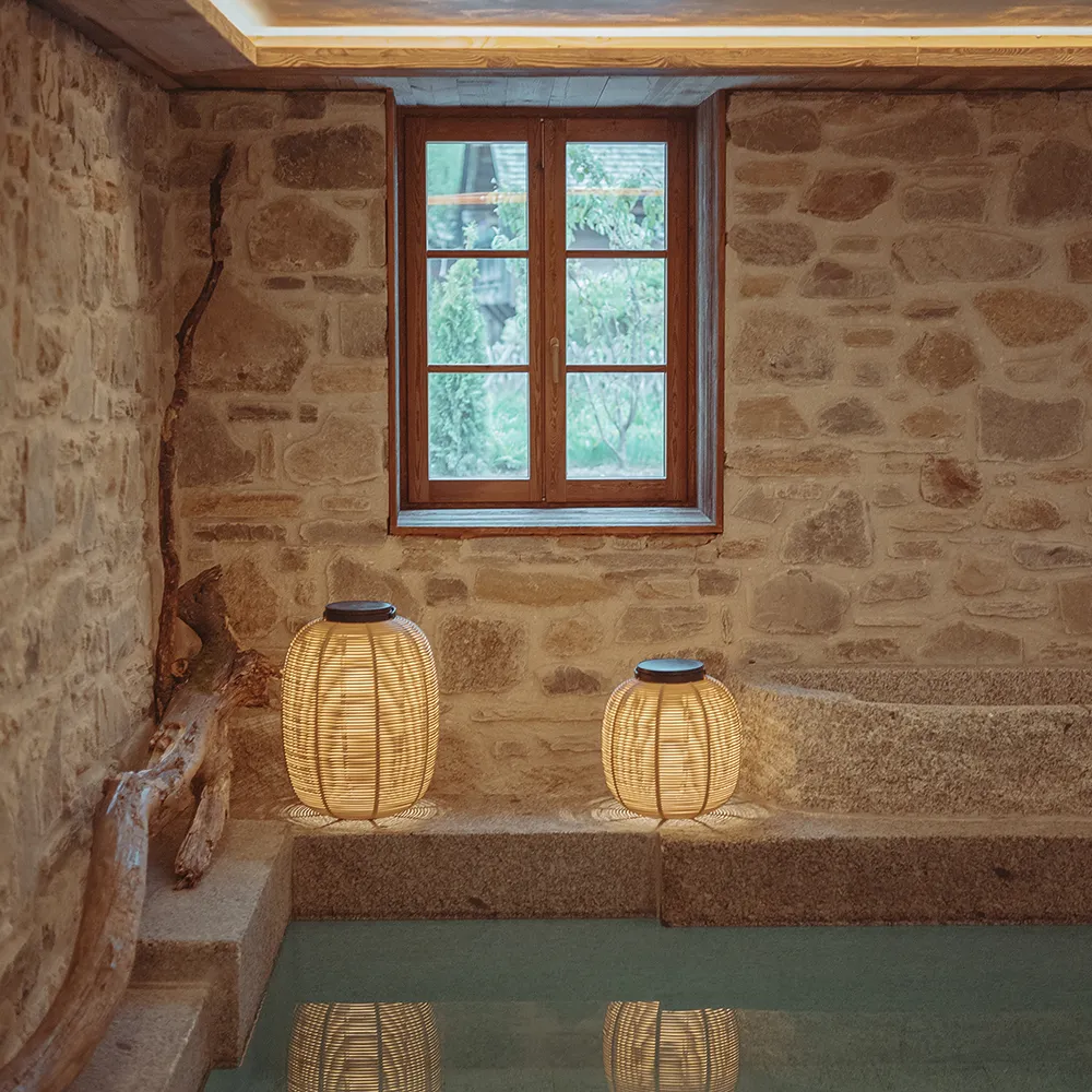 Intérieur en pierre avec fenêtre en bois et deux lanternes lumineuses posées près d'une piscine intérieure, La Ferme des Drus, Chamonix-Mont-Blanc, France.