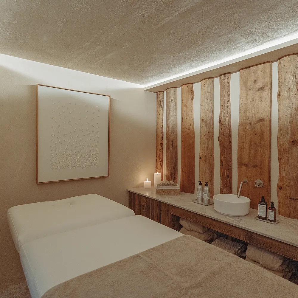 Salle de massage avec lits blancs, serviettes, bougies allumées et décor en bois naturel au mur, La Ferme des Drus, Chamonix-Mont-Blanc, France.