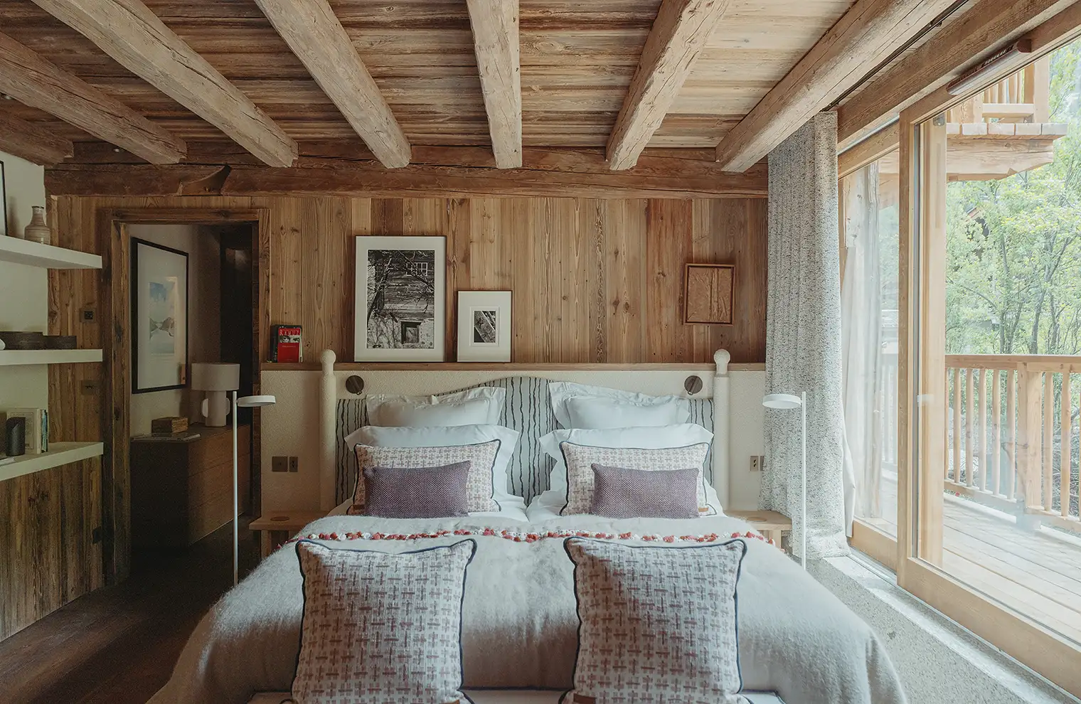 Chambre avec lit double, murs et plafond en bois, grandes fenêtres donnant sur un balcon en bois, La Ferme des Drus, Chamonix-Mont-Blanc, France.