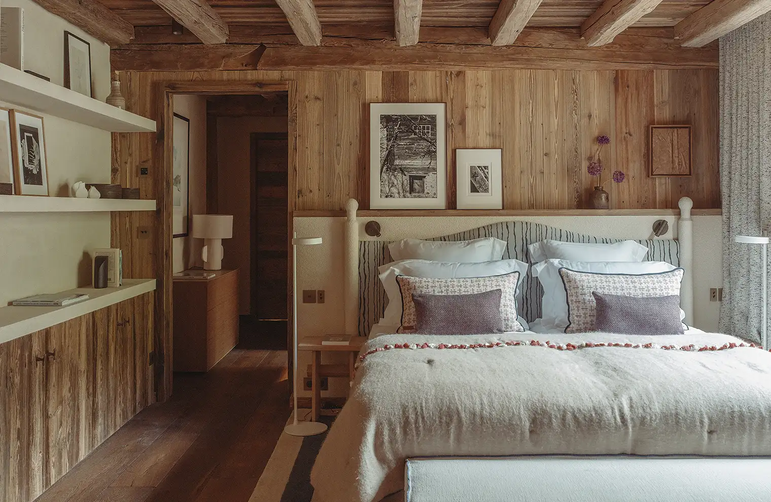 Chambre chaleureuse en bois avec lit double, coussins décoratifs et étagères avec cadres photo, La Ferme des Drus, Chamonix-Mont-Blanc, France.