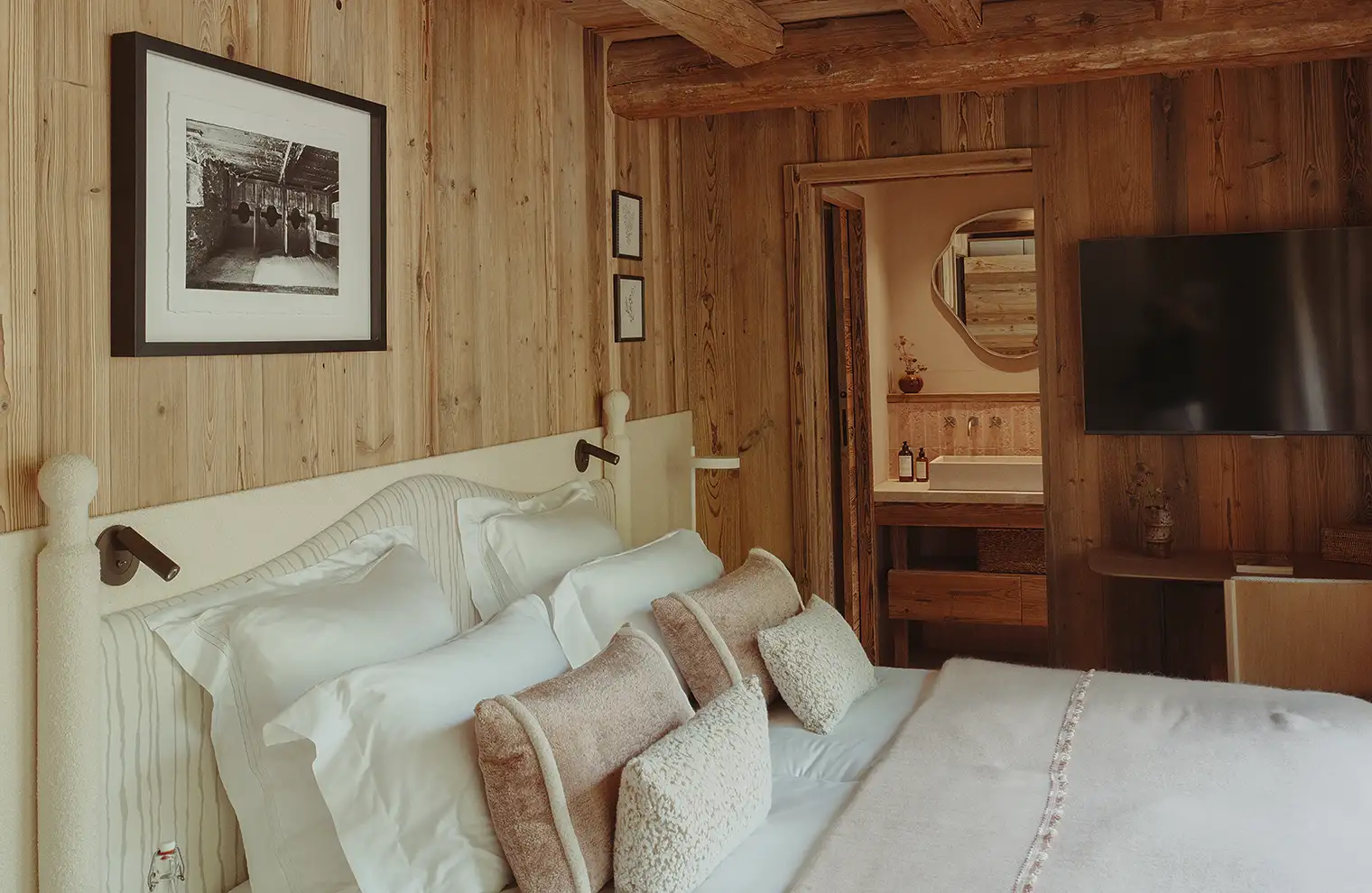 Chambre douillette en bois avec lit blanc, coussins beige, télévision murale et lavabo visible, La Ferme des Drus, Chamonix-Mont-Blanc, France, La Ferme des Drus, Chamonix-Mont-Blanc, France.