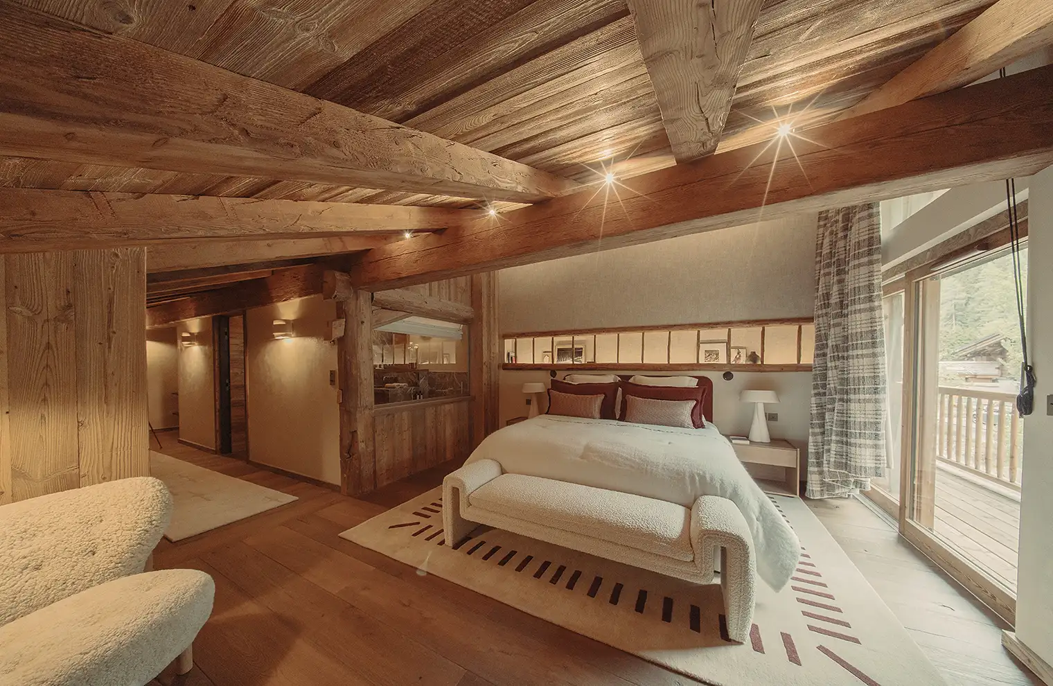 Chambre chaleureuse avec poutres en bois, lit double, fauteuils blancs et balcon extérieur, La Ferme des Drus, Chamonix-Mont-Blanc, France.