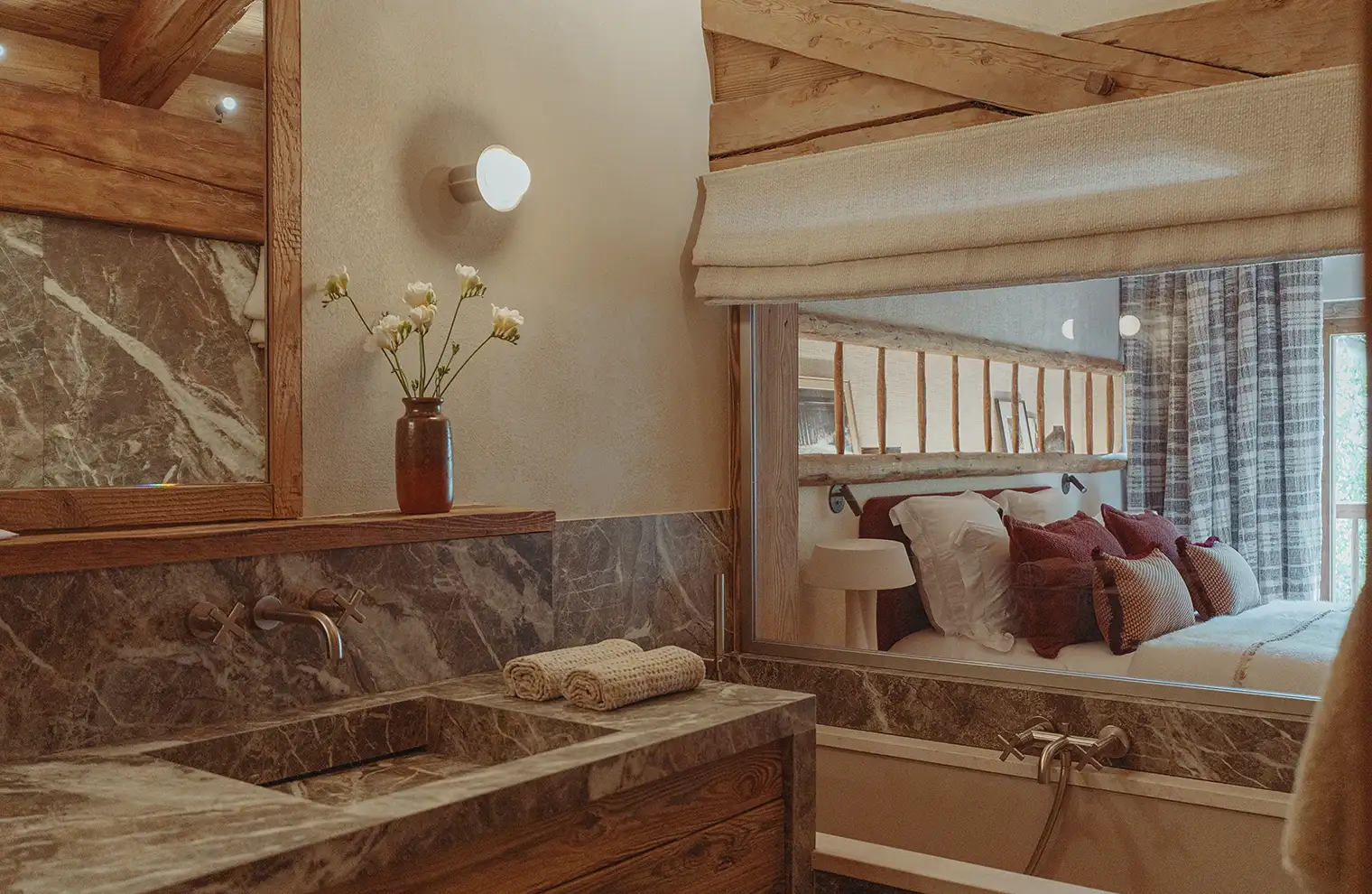 Salle de bain en marbre avec vasque intégrée, serviettes pliées, vase à fleurs et vue sur une chambre, La Ferme des Drus, Chamonix-Mont-Blanc, France.