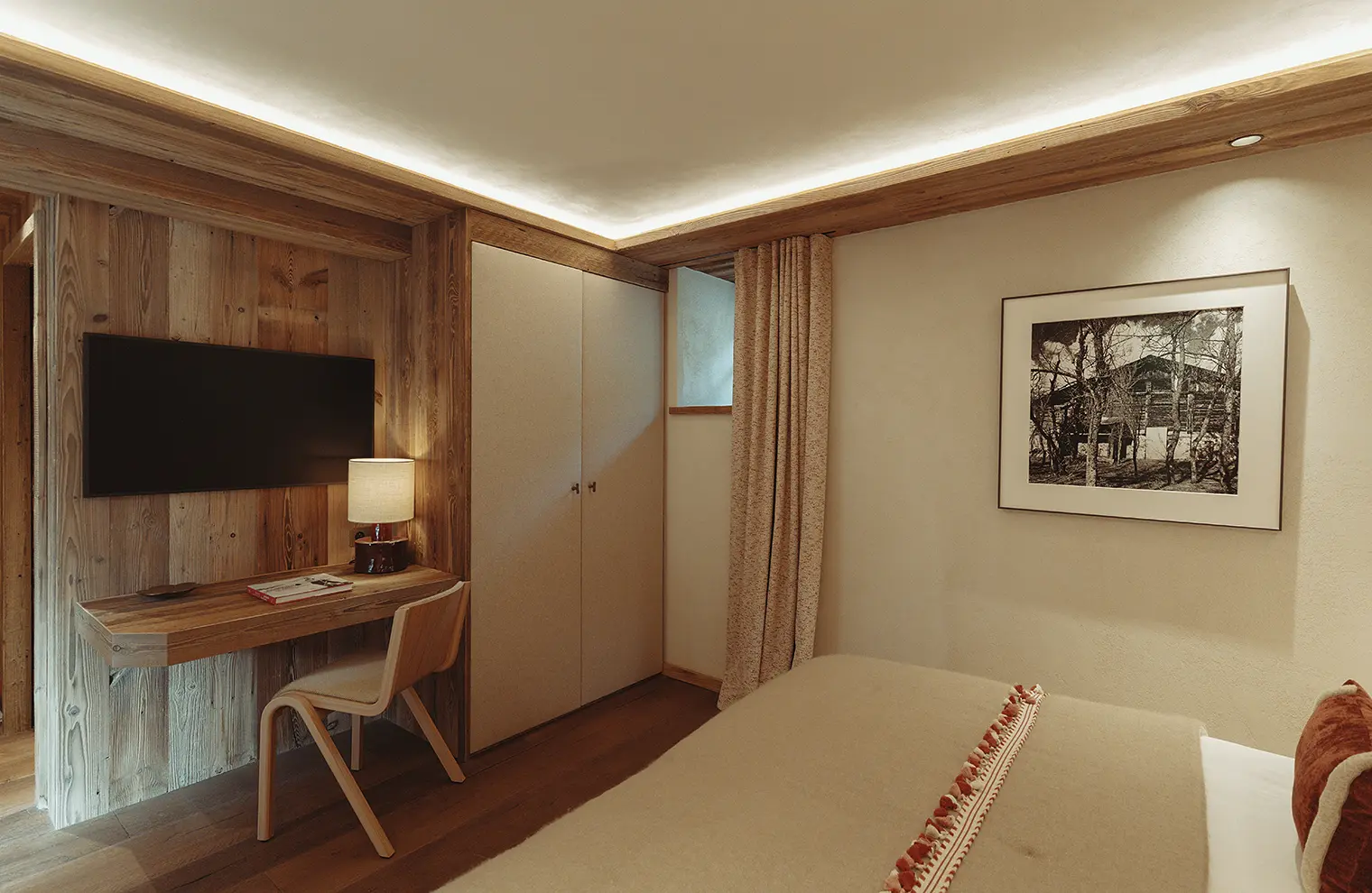 Chambre avec mur en bois, télé murale, bureau avec lampe, lit, armoire et cadre photo, La Ferme des Drus, Chamonix-Mont-Blanc, France.