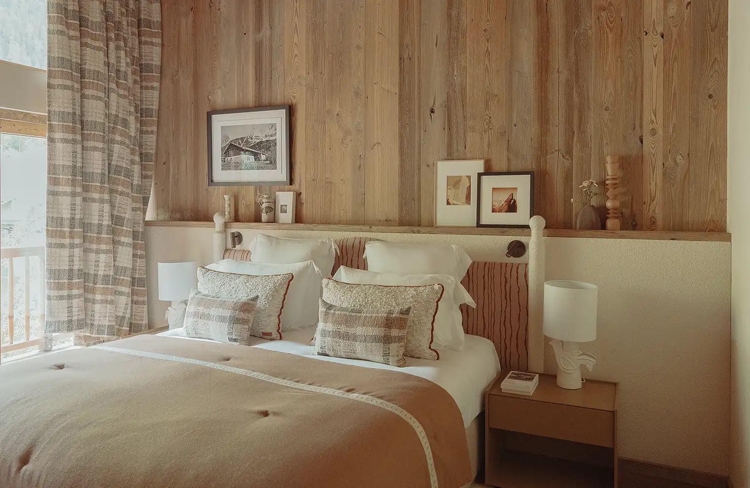 Chambre avec lit double, coussins décoratifs, couvre-lit beige et mur en bois avec cadres photo, La Ferme des Drus, Chamonix-Mont-Blanc, France.