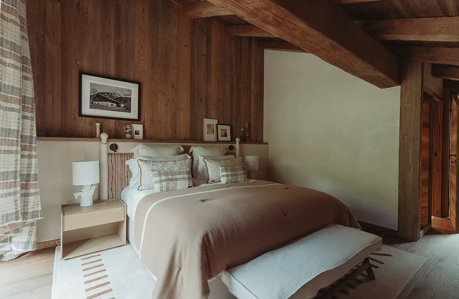 Chambre à coucher rustique avec mur en bois, grande couette beige et coussins décoratifs, La Ferme des Drus, Chamonix-Mont-Blanc, France.