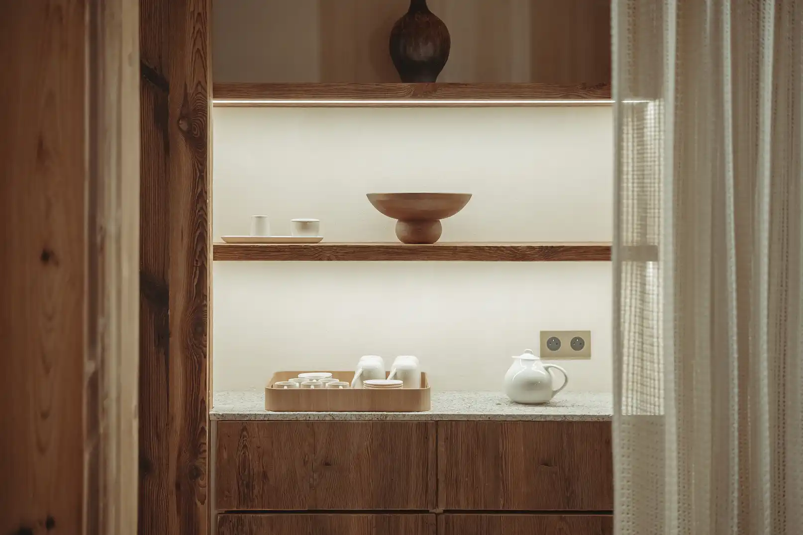 Cuisine avec étagères en bois, luminaire intégré, plateau de tasses et bouilloire blanche posée sur le comptoir, La Ferme des Drus, Chamonix-Mont-Blanc, France.