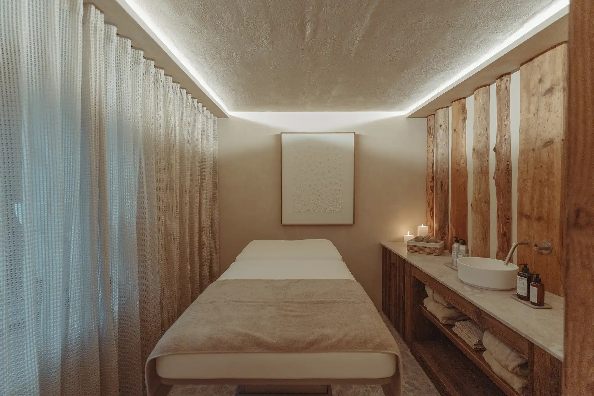 Salle de massage calme avec table, rideaux, lumière douce, lavabo et serviettes, La Ferme des Drus, Chamonix-Mont-Blanc, France.