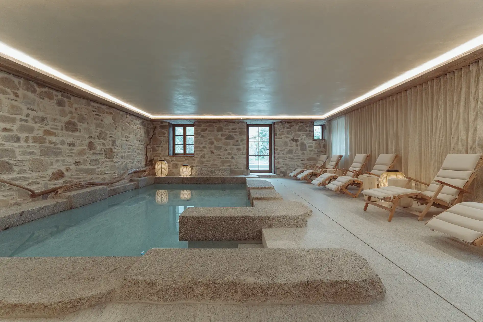 Piscine intérieure avec murs en pierre, chaises longues beige et éclairage doux au plafond, La Ferme des Drus, Chamonix-Mont-Blanc, France.