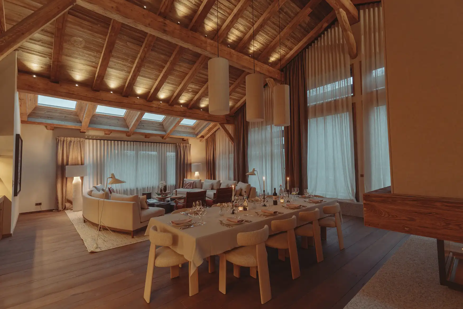 Salon avec plafond en bois, grande table à manger dressée et canapés confortables sous des luminaires suspendus, La Ferme des Drus, Chamonix-Mont-Blanc, France.