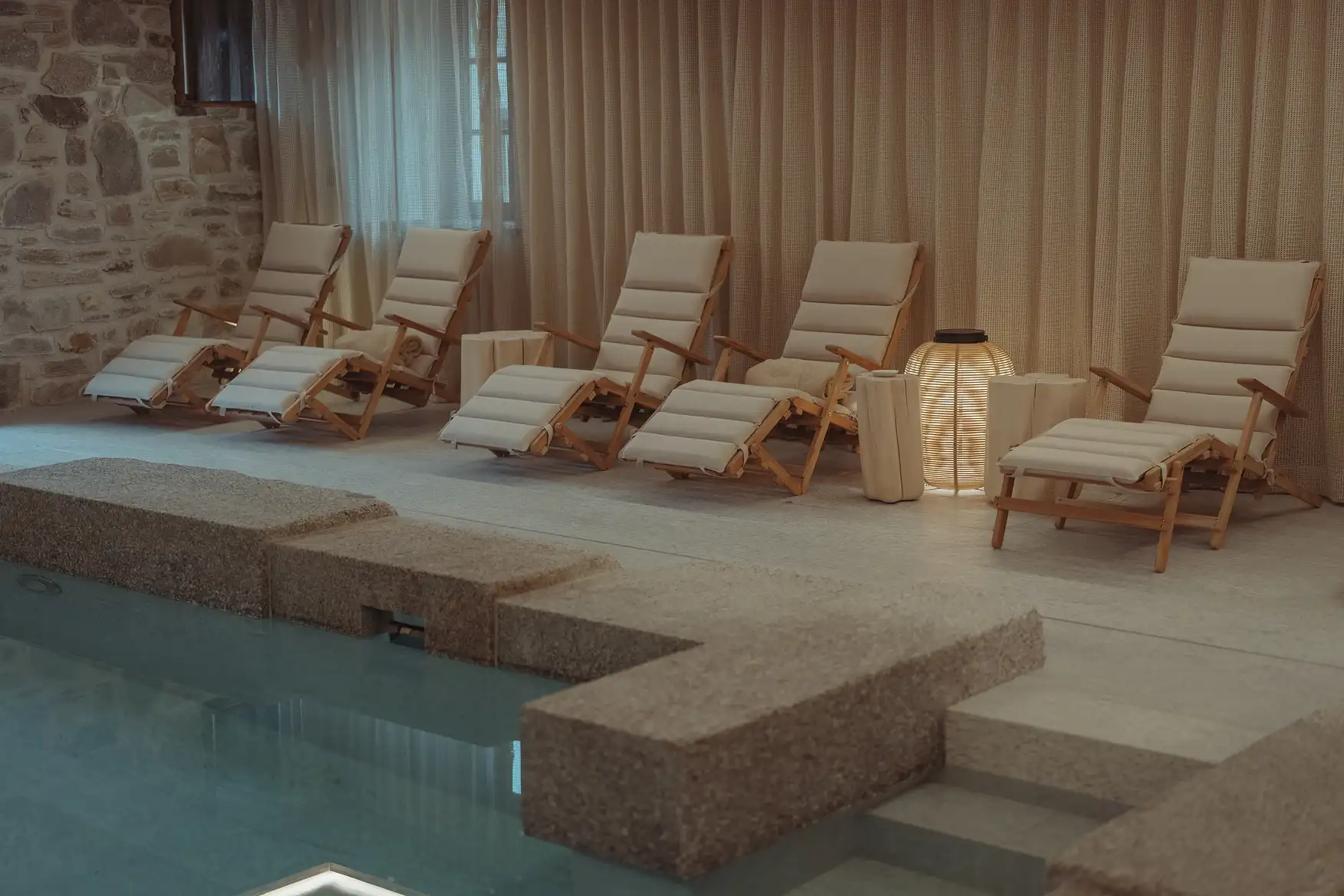 Cinq chaises longues crème en bois alignées près d'une piscine intérieure dans une ambiance zen, La Ferme des Drus, Chamonix-Mont-Blanc, France.