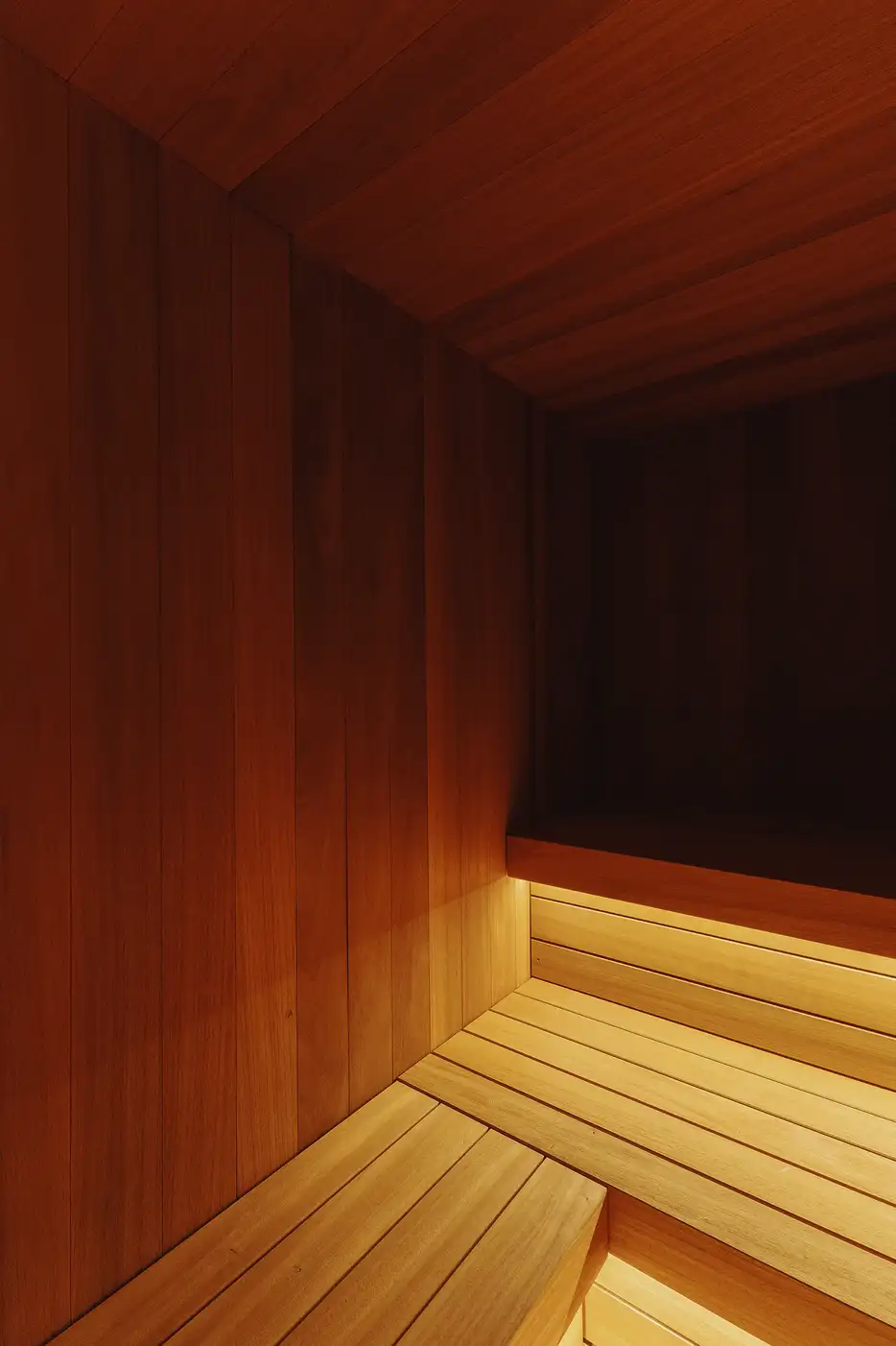 Intérieur chaleureux d'un sauna en bois avec bancs et éclairage tamisé sous les sièges, La Ferme des Drus, Chamonix-Mont-Blanc, France.