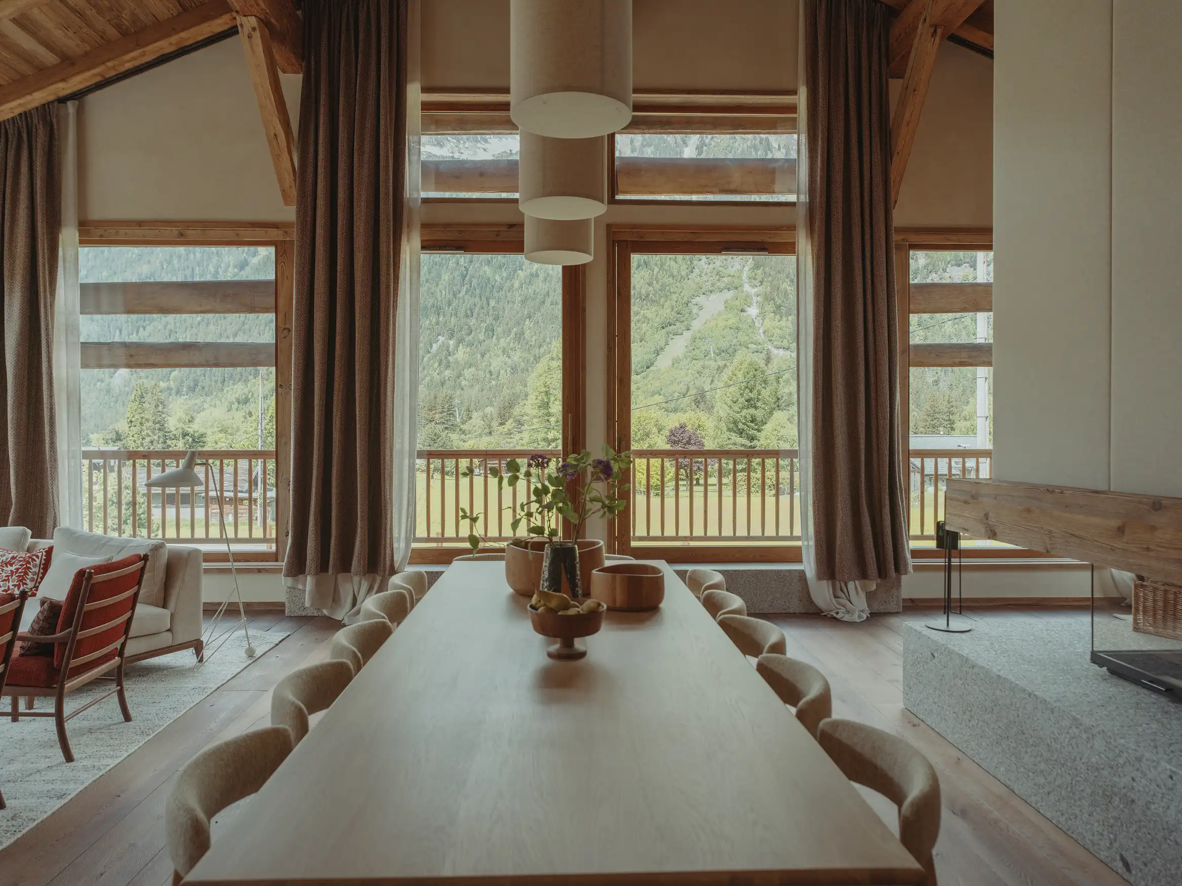 Salle à manger avec grande table en bois et vue sur montagne à travers de grandes fenêtres, La Ferme des Drus, Chamonix-Mont-Blanc, France.