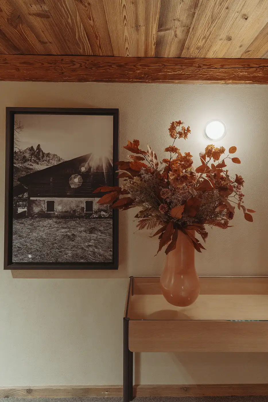 Bouquet de fleurs séchées dans un vase orange sur une console près d'une photo encadrée, La Ferme des Drus, Chamonix-Mont-Blanc, France.