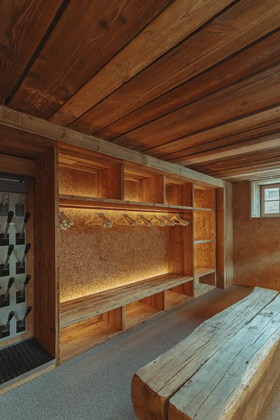 Vestiaire en bois avec patères, cintres et banc brut sous un plafond en bois, La Ferme des Drus, Chamonix-Mont-Blanc, France.