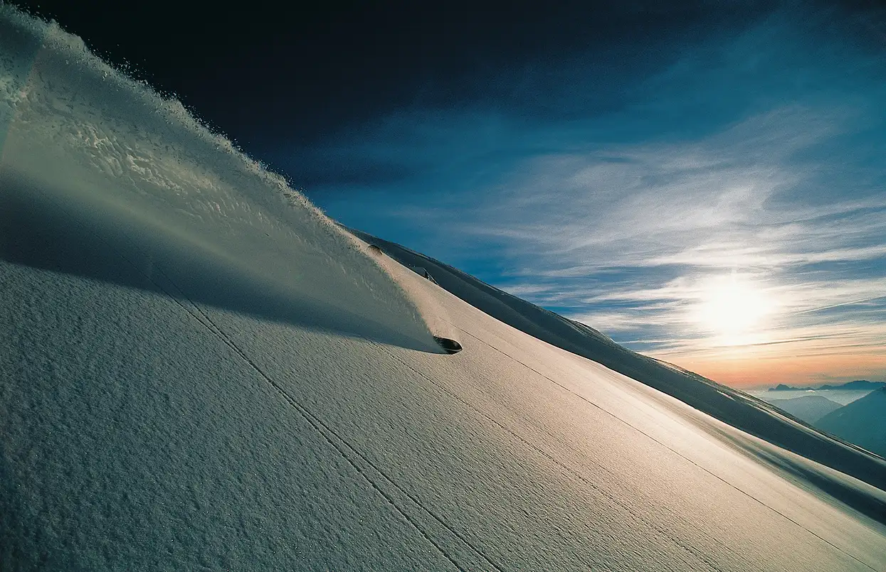 Skieur descendant une pente enneigée avec une traînée poudreuse au coucher du soleil, La Ferme des Drus, Chamonix-Mont-Blanc, France.