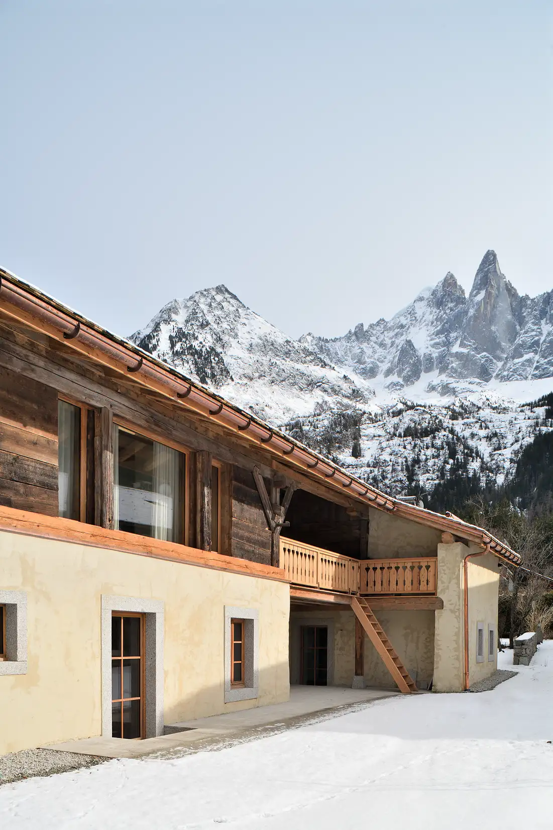 Maison en bois et pierre avec neige au sol, montagnes enneigées en arrière-plan, La Ferme des Drus, Chamonix-Mont-Blanc, France.