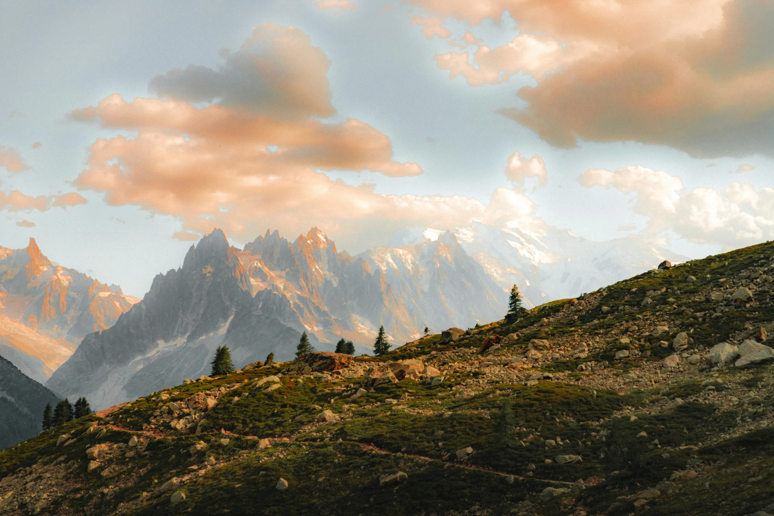 Montagnes rocheuses avec pins sur une colline verdoyante sous un ciel nuageux au coucher du soleil, La Ferme des Drus, Chamonix-Mont-Blanc, France.
