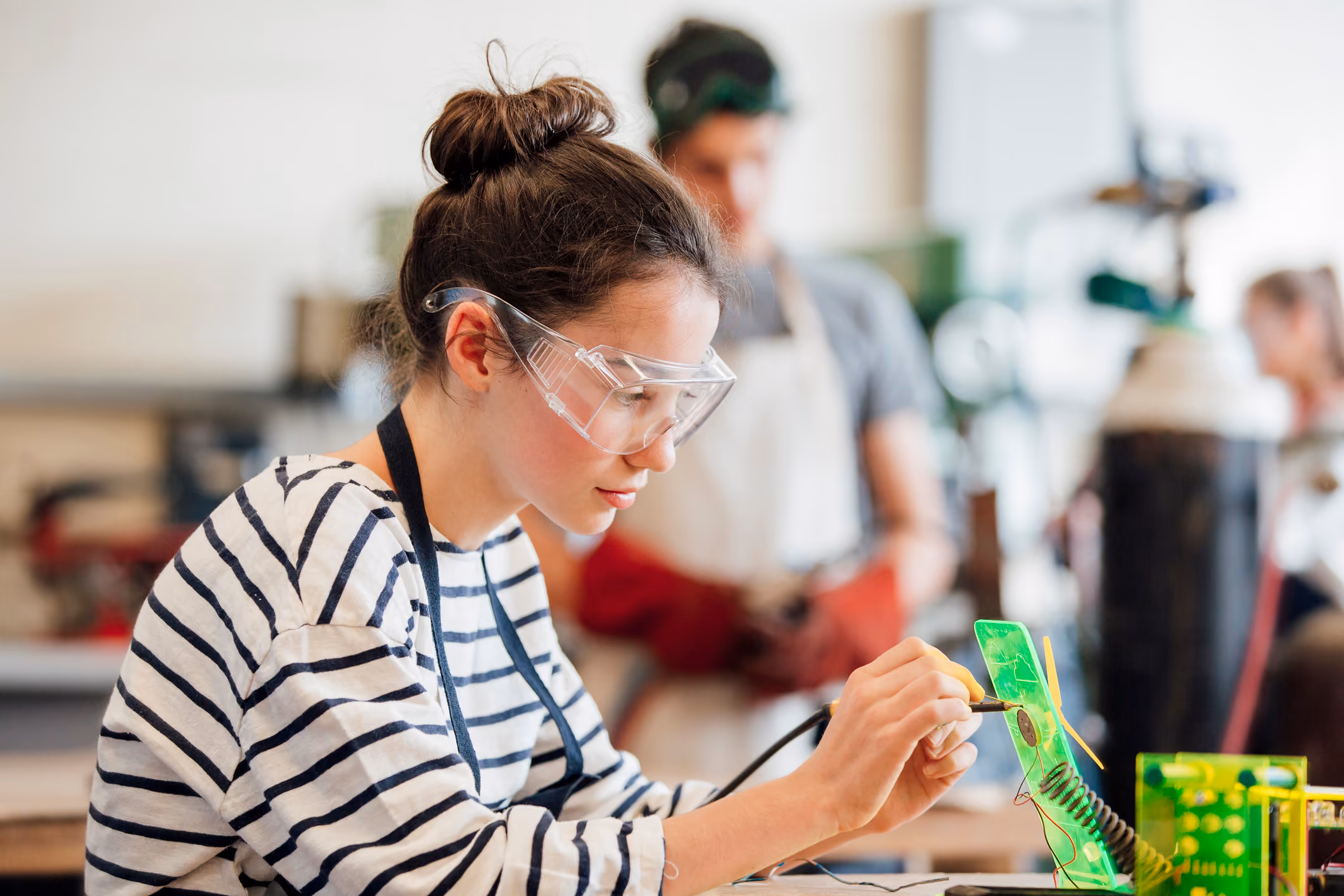 Une lycéenne soude un circuit électronique en atelier, sous la supervision d'un enseignant