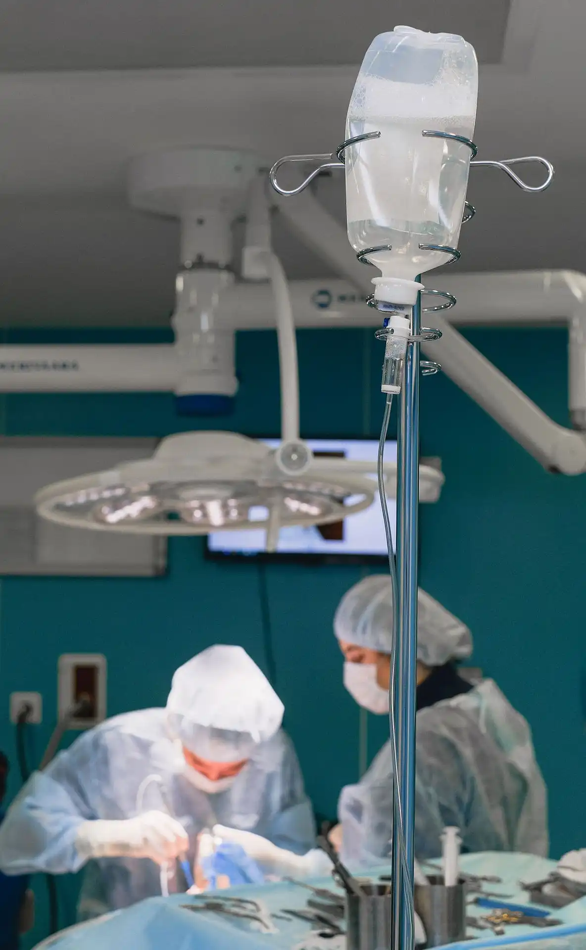 Infusionsflasche in einem Operationssaal mit Chirurgen, die eine Operation durchführen.