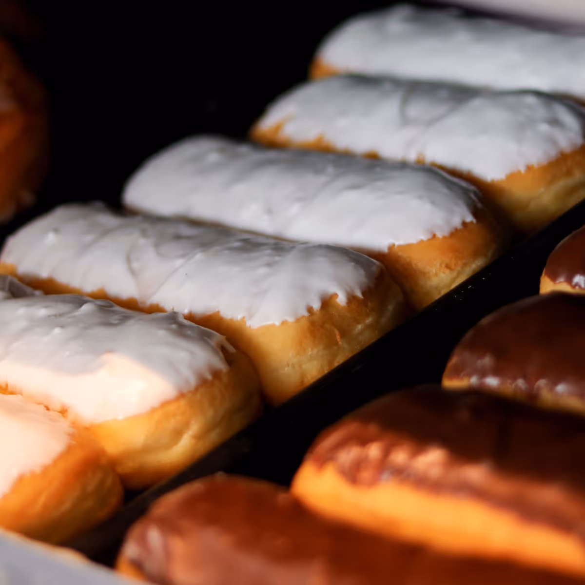 Tray of rectangular éclairs topped with white icing in the background and chocolate icing in the foreground.