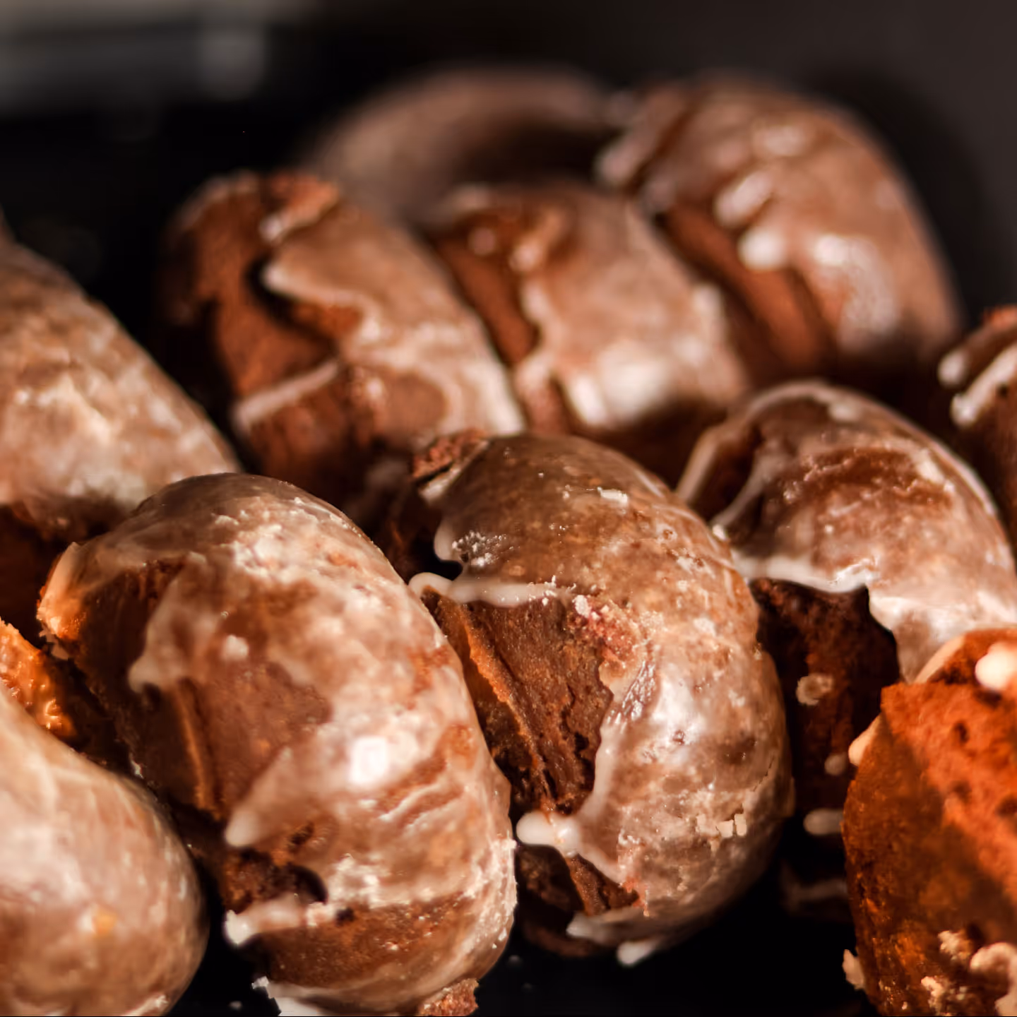 Close-up of glazed chocolate cake donuts arranged on a dark surface.