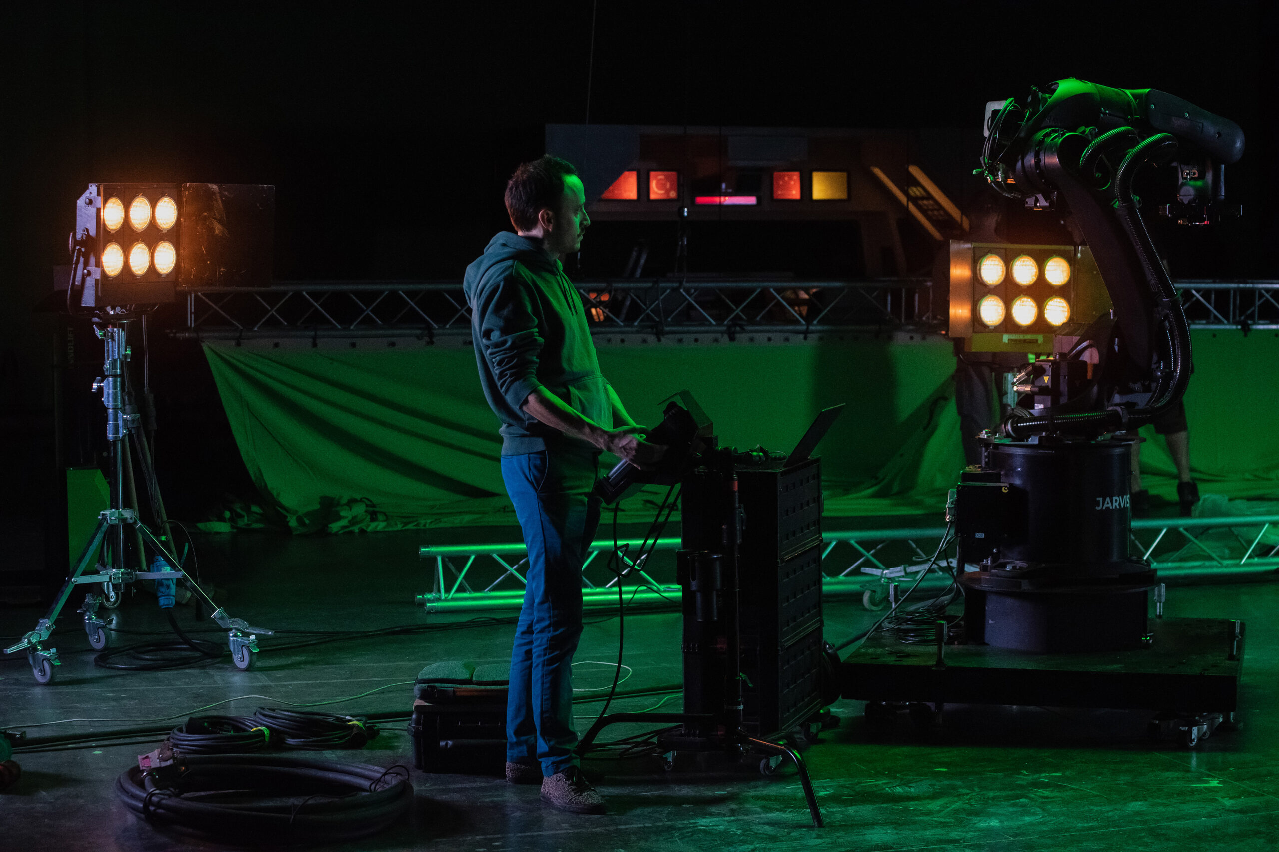 Technician setting up equipment on a green screen stage under green lighting