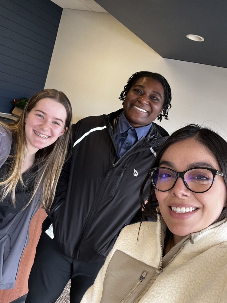 Three smiling patients posing together inside a modern dental office creating a warm and welcoming atmosphere