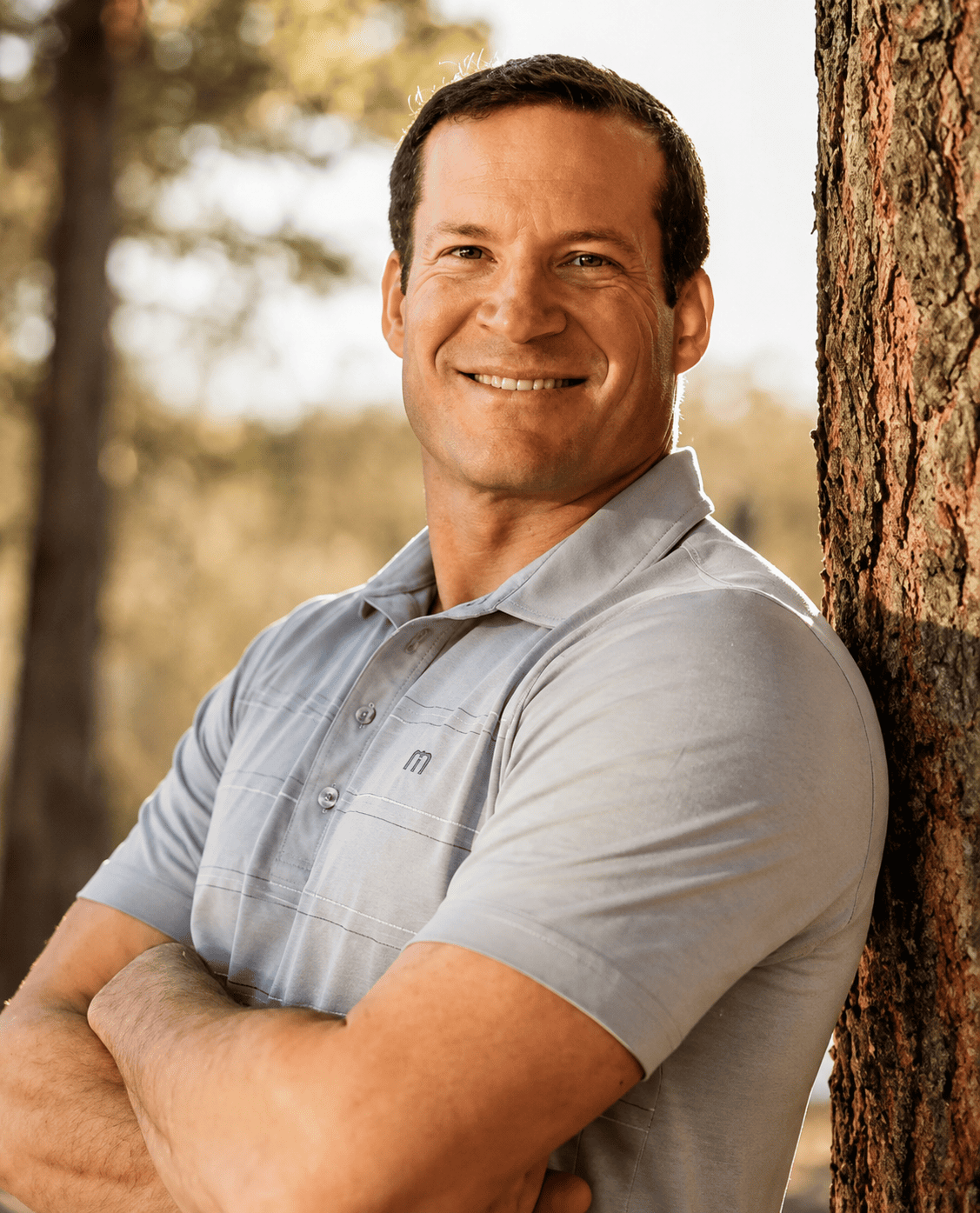 Portrait of Dr Scott R Hill smiling outdoors beside a tree with a forest background