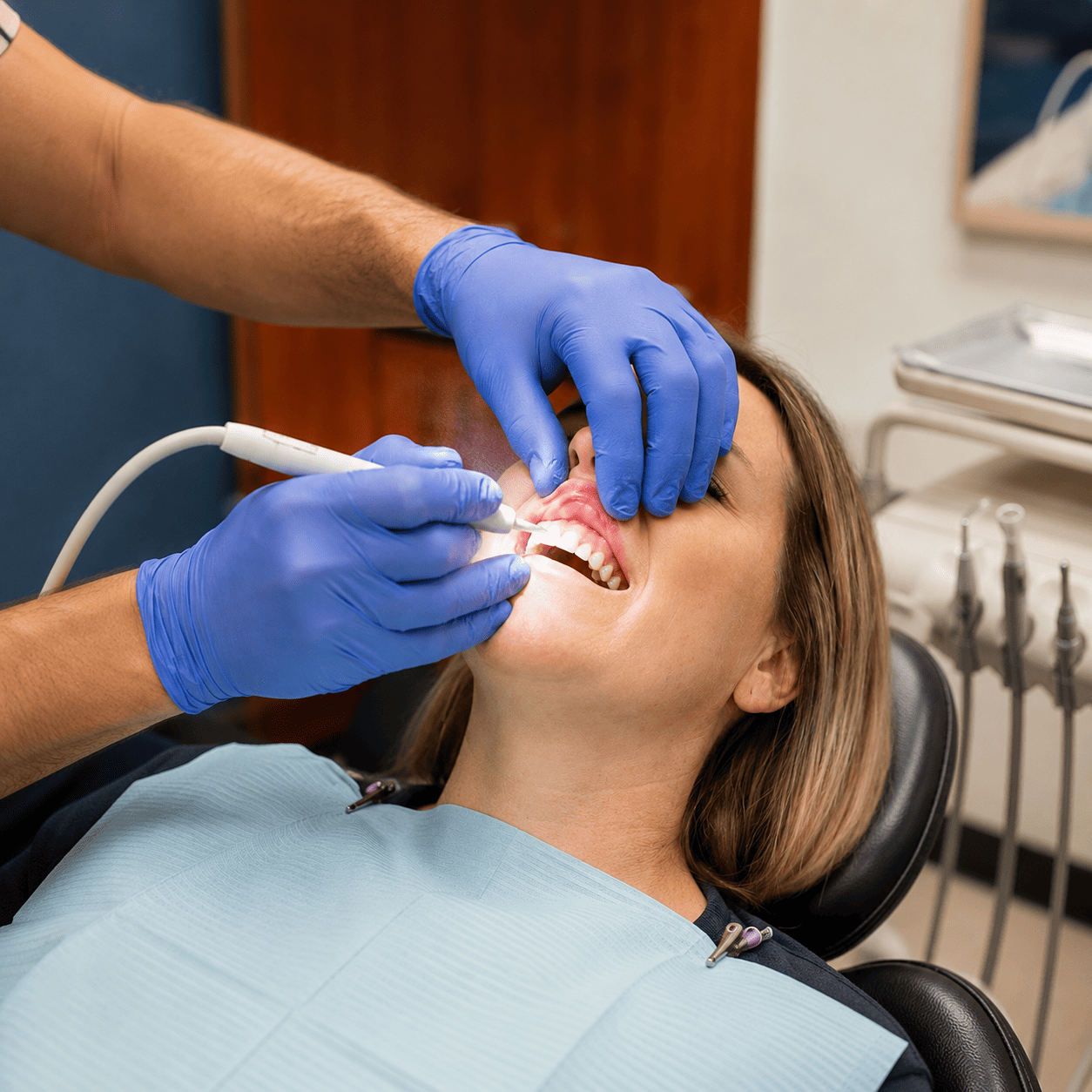 Dentist's gloved hands use an ultrasonic scaler to treat a patient's gum disease, showing inflamed gum tissue during therapy.
