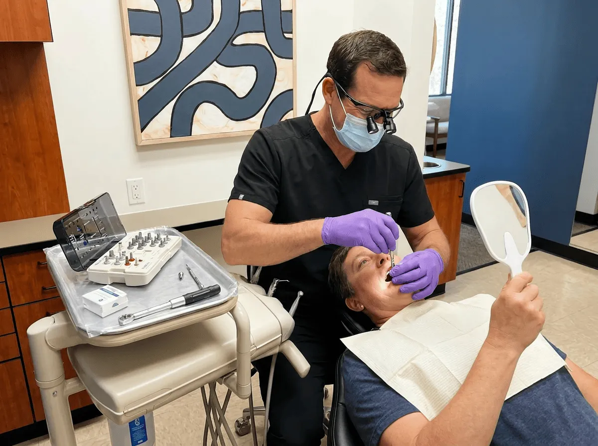 Dentist threads All-on-4 implant abutment as patient watches through mirror in a restorative operatory.
