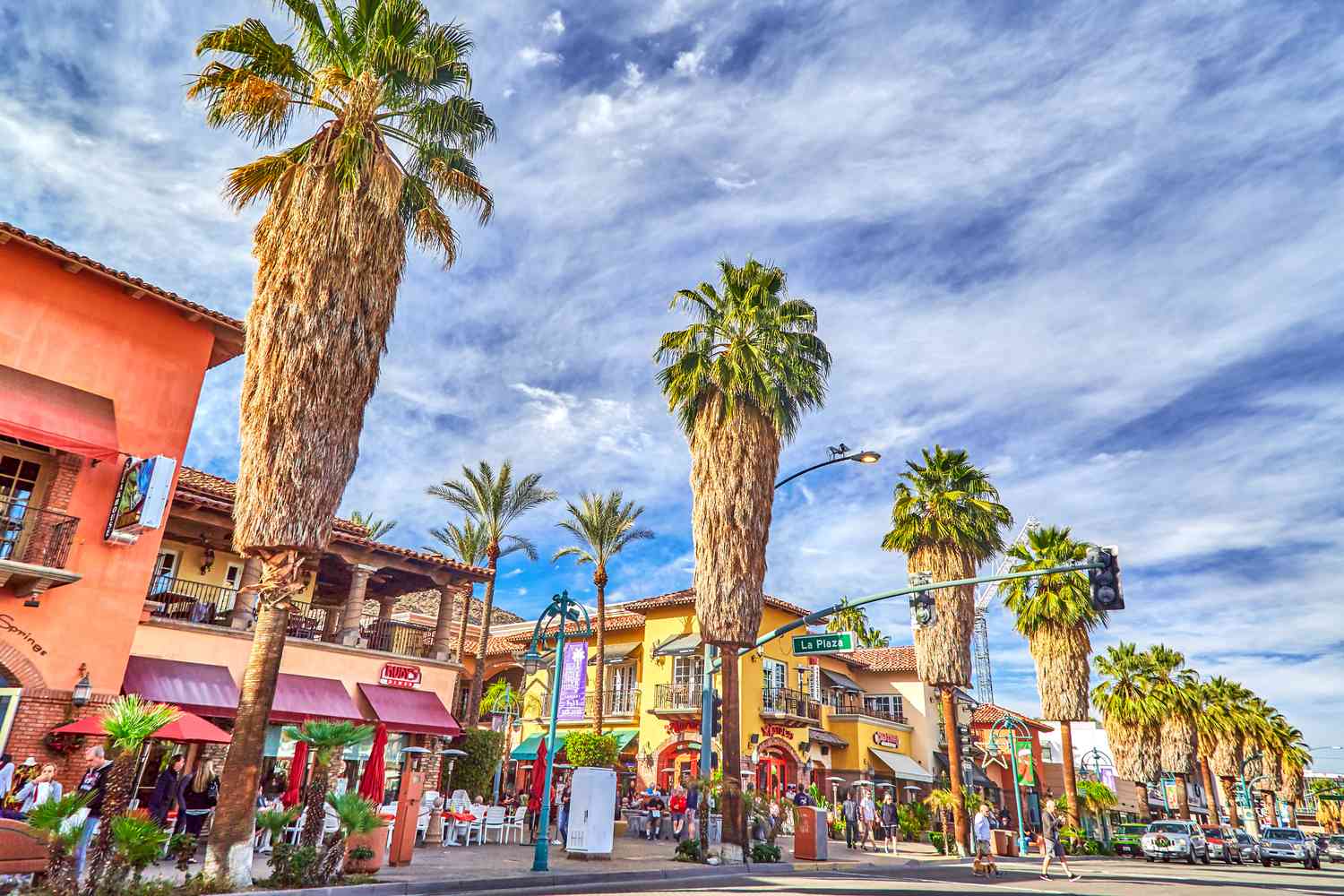 Street scene with tall palm trees, colorful buildings, and people walking on a sunny day.