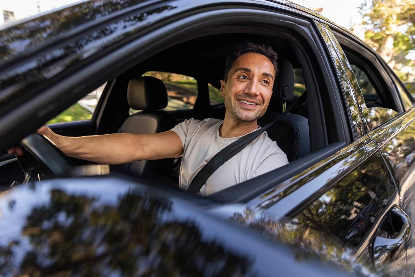 Man with a red beard smiling inside a car, seated behind the steering wheel with dashboard visible.